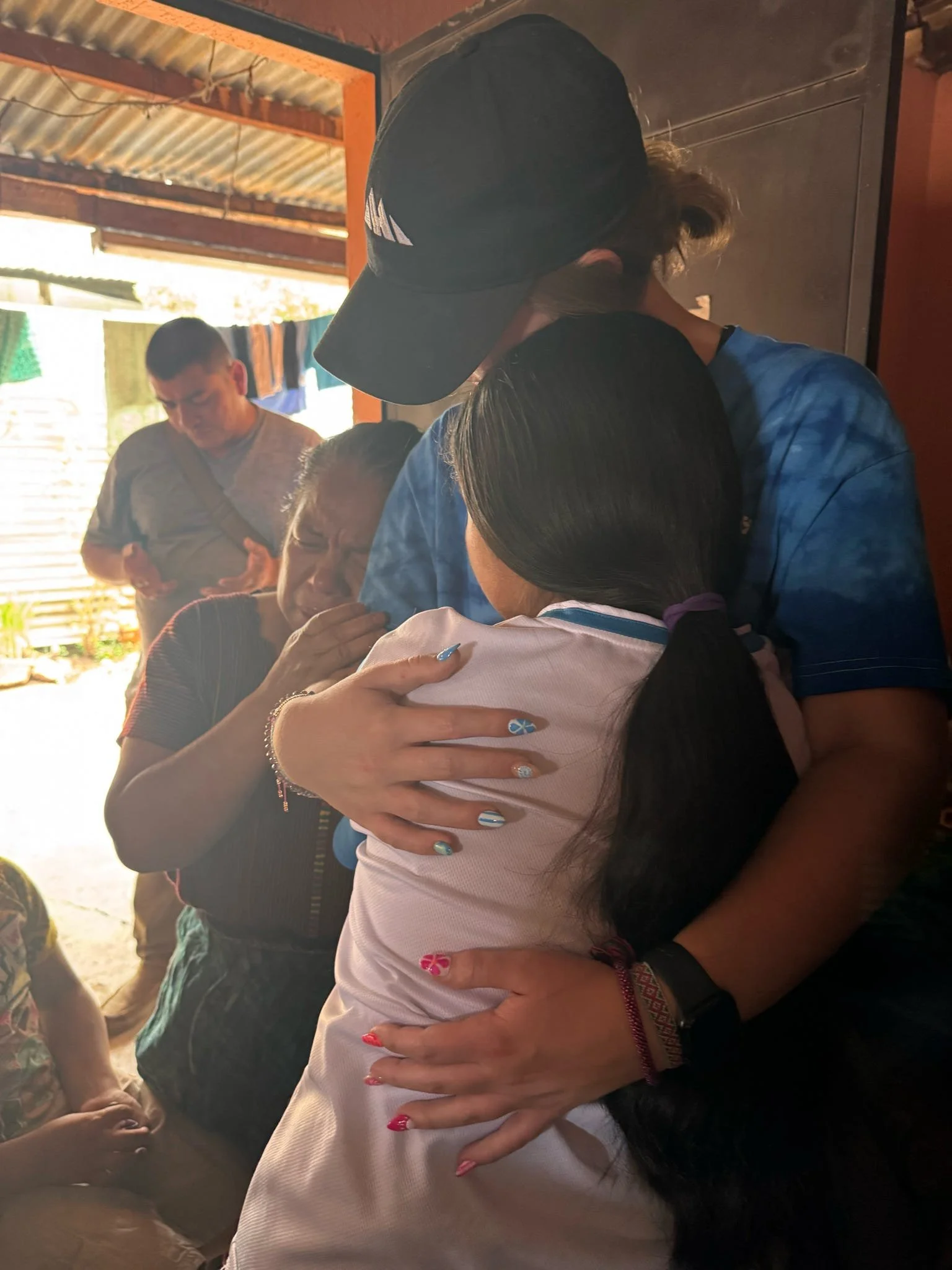 A group of people sharing a heartfelt hug, inside a rustic building with natural light coming in.