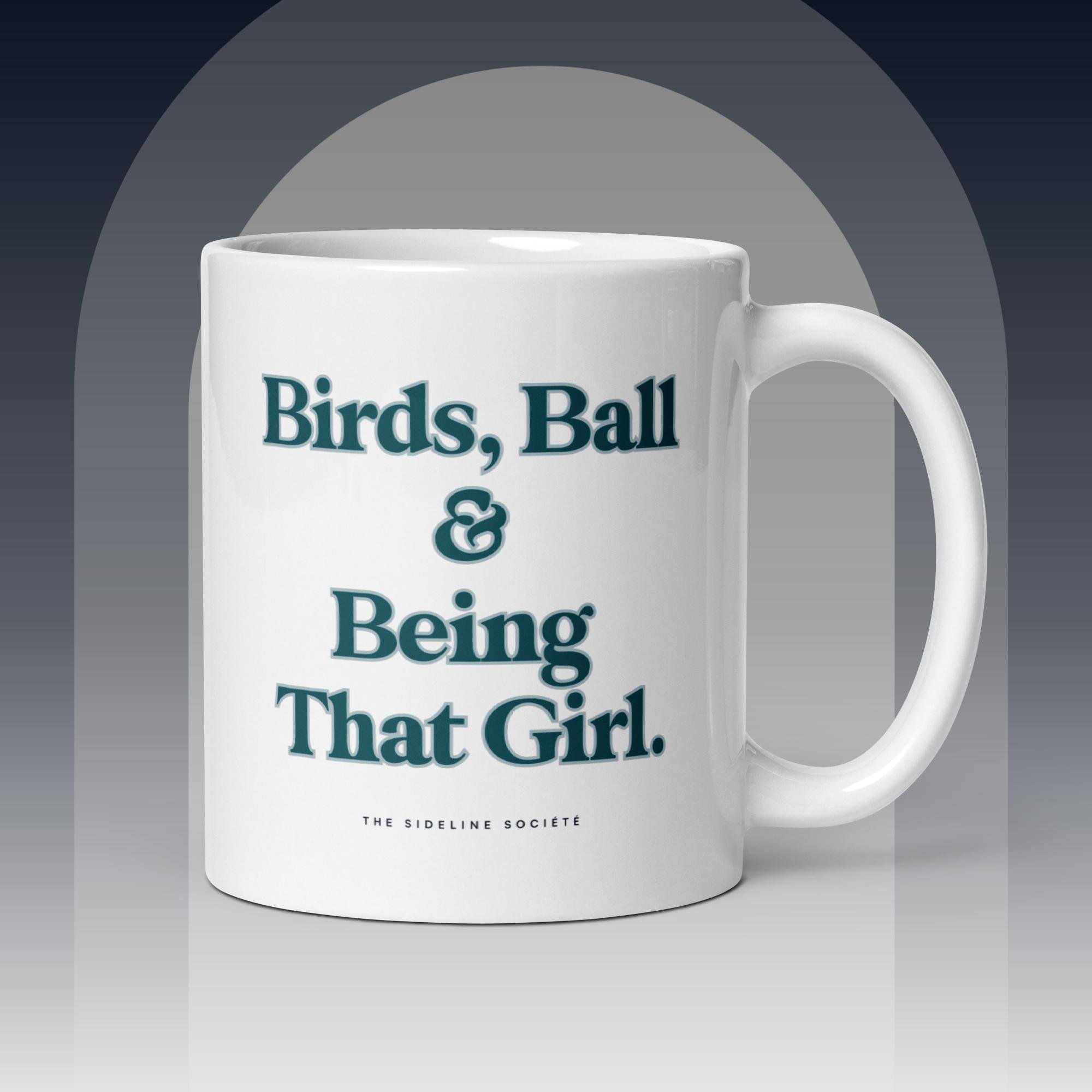 White ceramic coffee mug with green text reading “Birds, Ball & Being That Girl” by The Sideline Société
