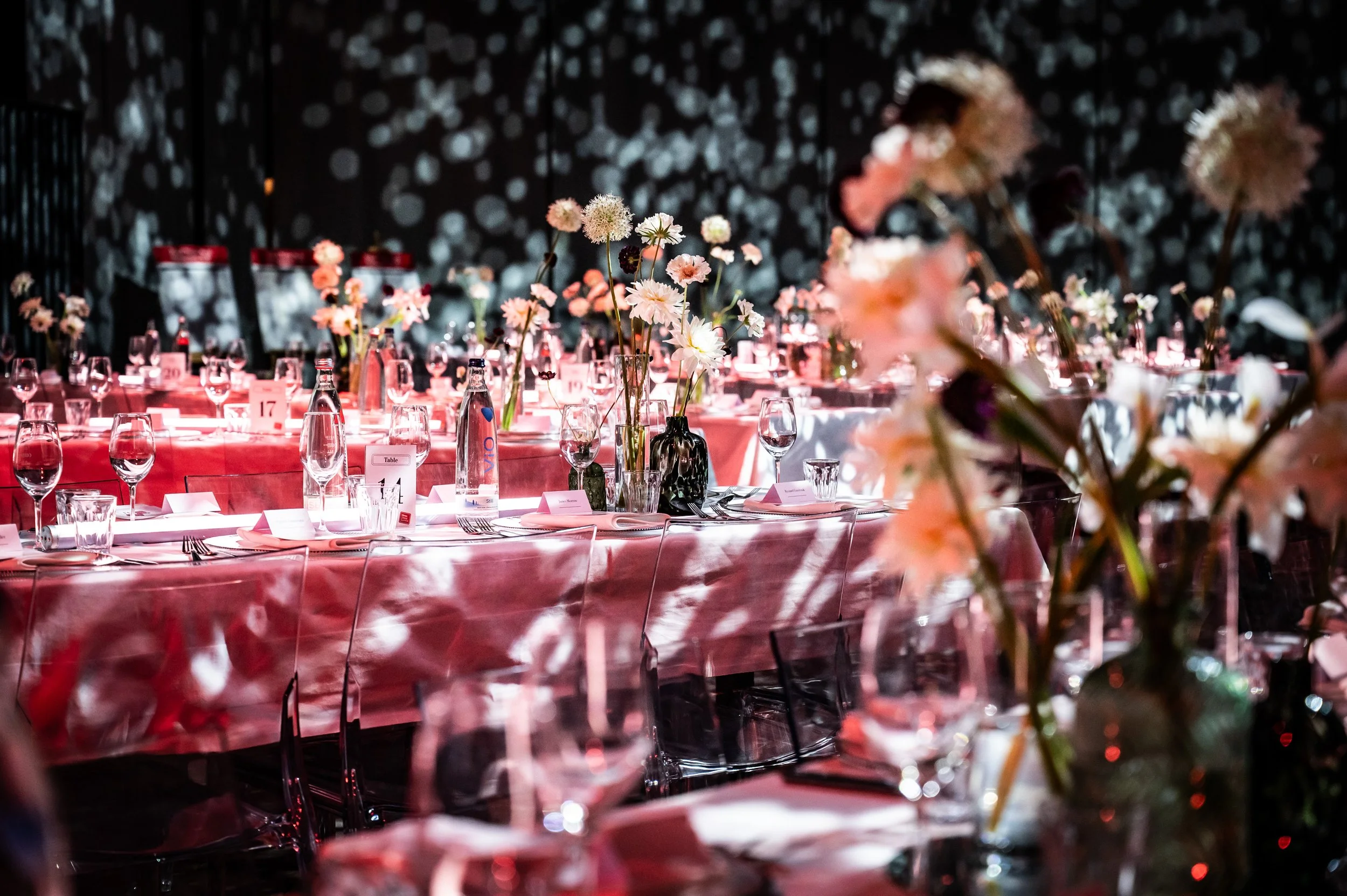 Eleganter Festsaal mit gedeckten Tischen, Blumenarrangements und Beleuchtung mit Schattenmustern an der Wand.