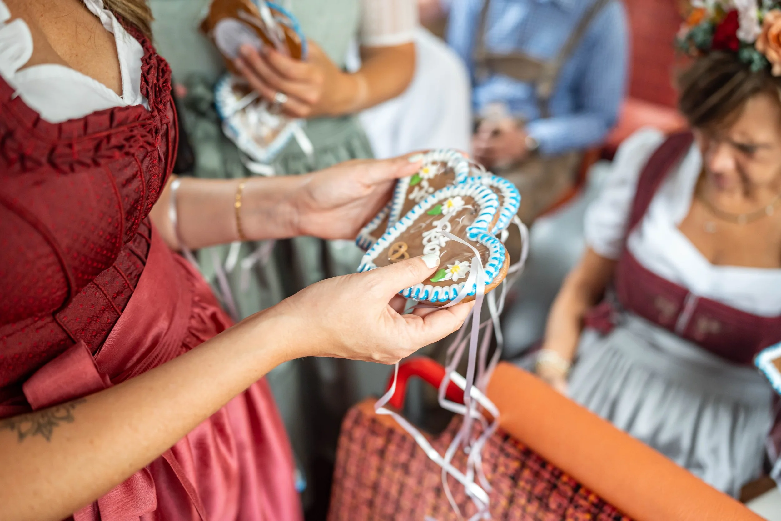 Mehrere Frauen halten Lebkuchenherzen, die mit Zuckerguss und Dekoration verziert sind, bei einem Fest. Die Frauen tragen traditionelle Trachten.