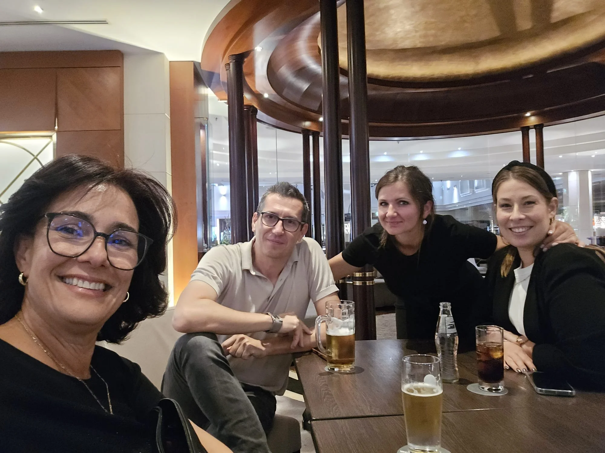 Vier Menschen sitzen an einem Tisch in einem Restaurant oder Bar, einige haben Getränke vor sich, alle lächeln in die Kamera.