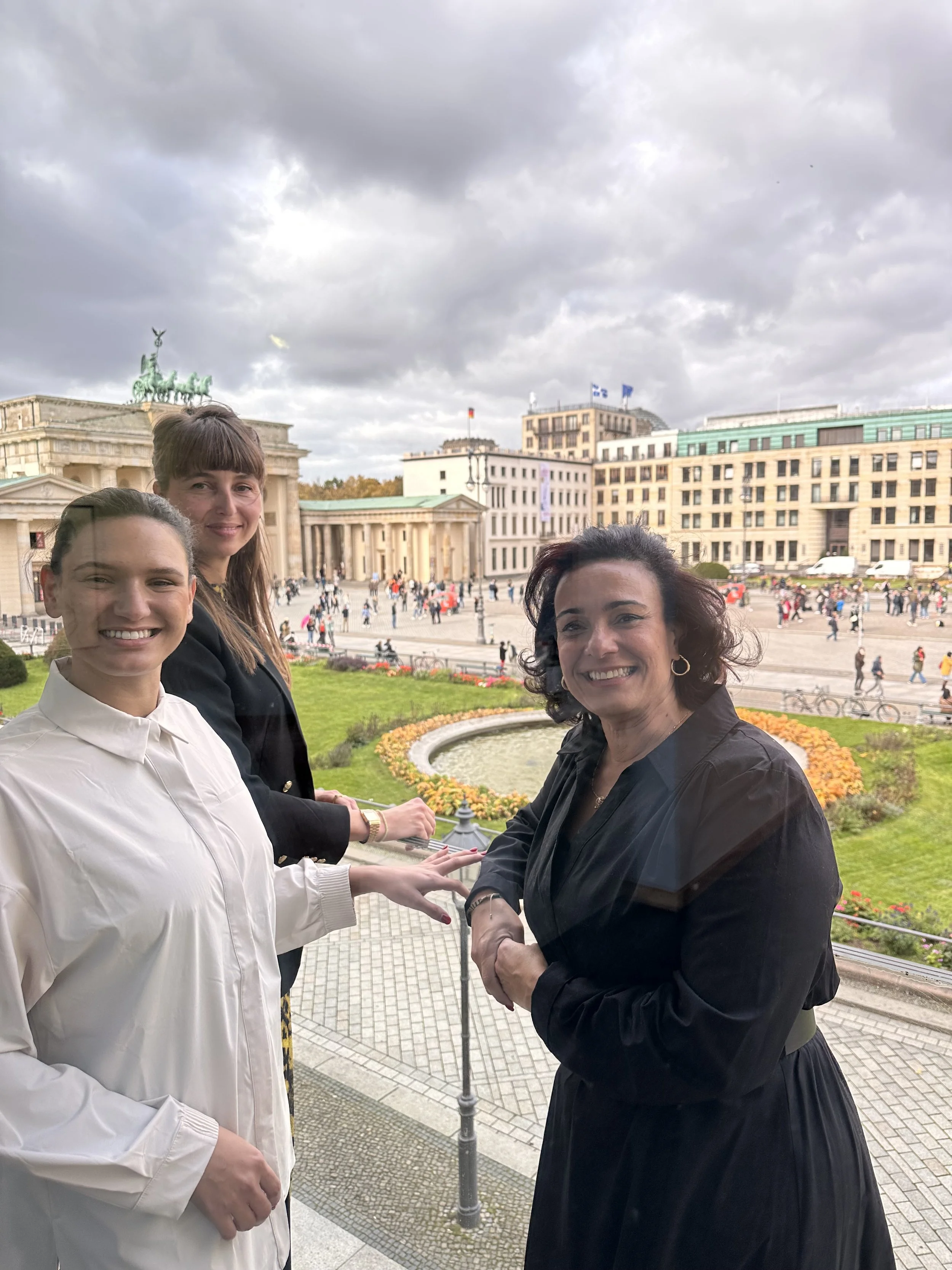 Drei Frauen stehen vor dem Brandenburger Tor in Berlin, Deutschland, mit einer belebten Stadt im Hintergrund.