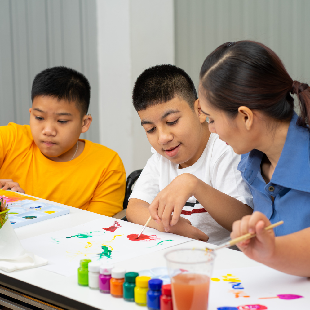 A woman teaching two young boys to paint with watercolors at a table.
