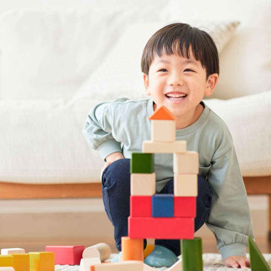 Young boy smiling and playing with colorful wooden building blocks indoors.