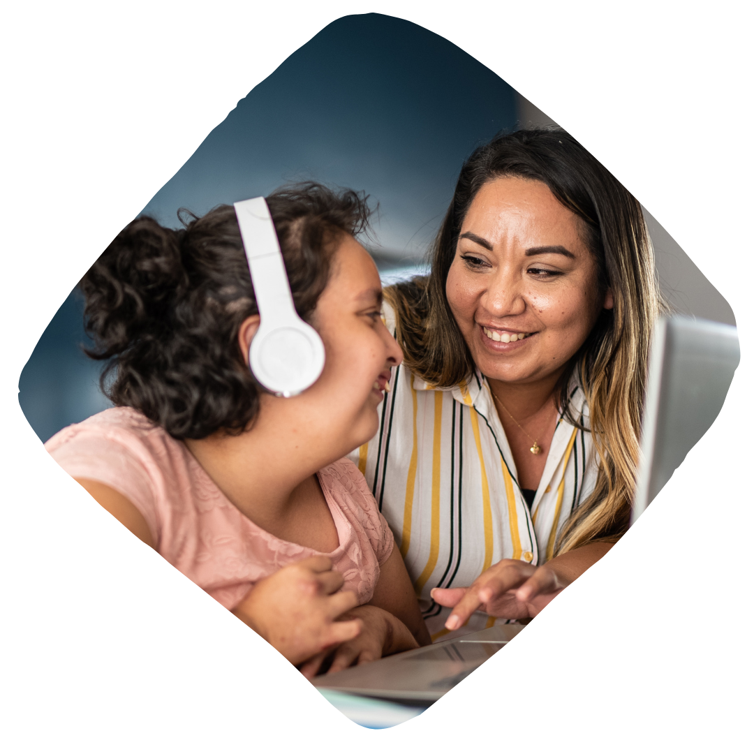 Two women smiling and engaging with each other, one wearing headphones and looking at a computer screen.