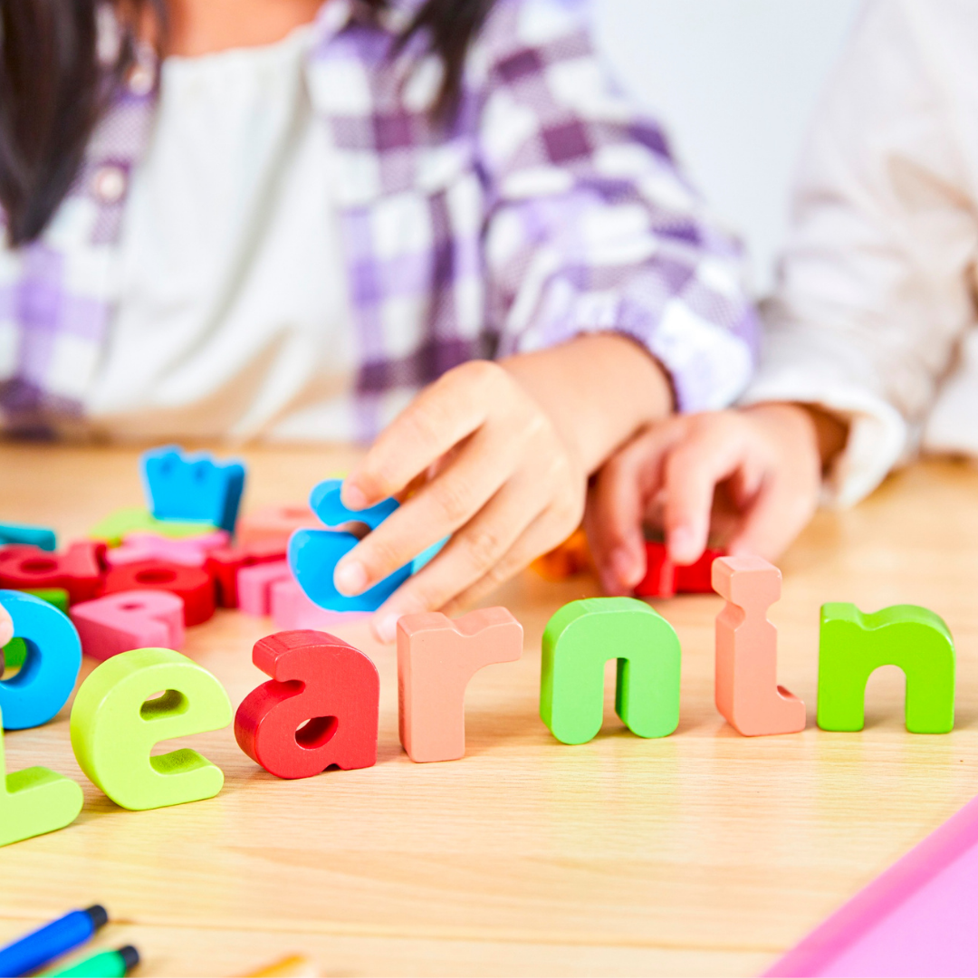 Person arranging colorful plastic alphabet letters spelling 'learning' on a wooden table.