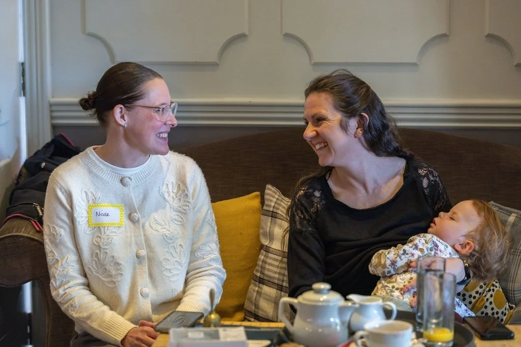 Two women at a network meeting, smiling, one holding a sleeping child