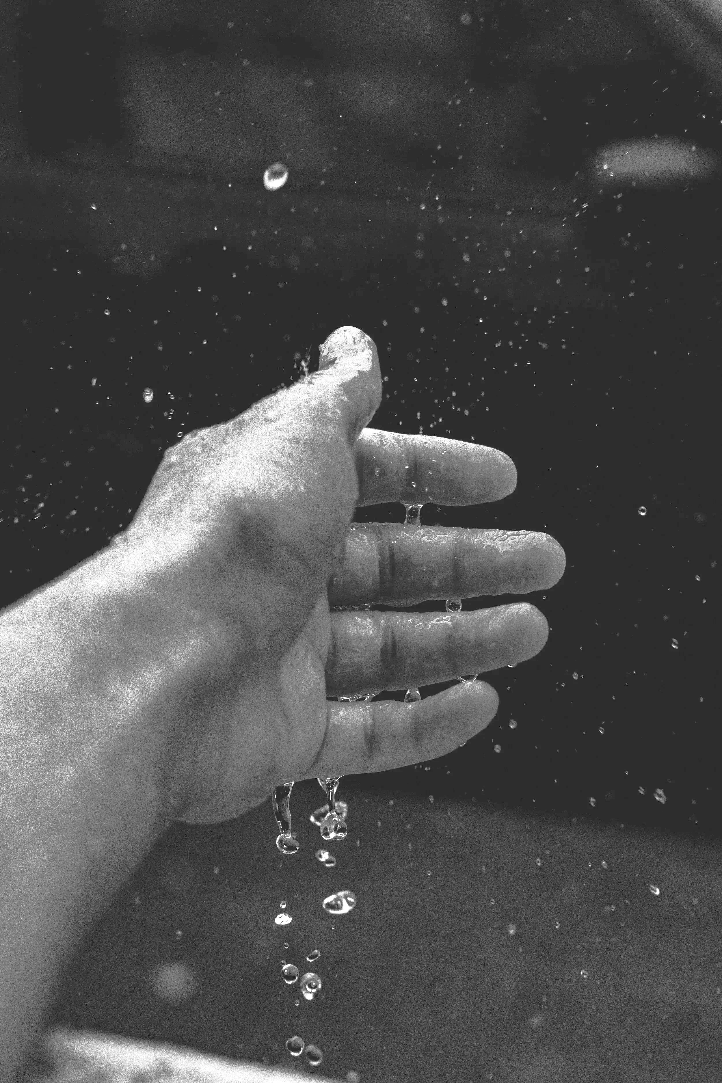 A black and white photo of a hand with water dripping from it, against a dark background.