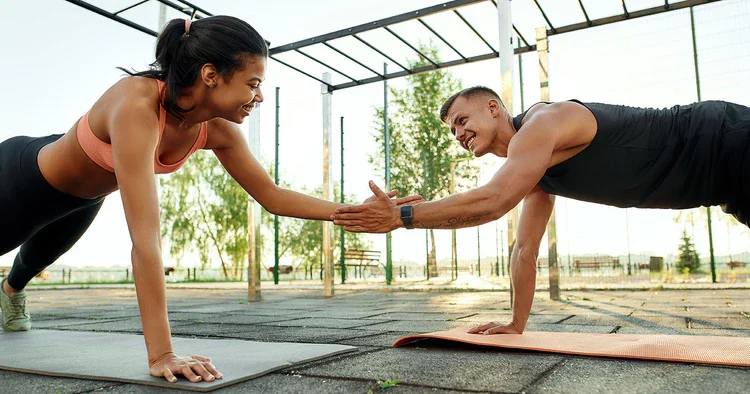 A man and woman doing a high-five during their workout on mats at an outdoor gym.