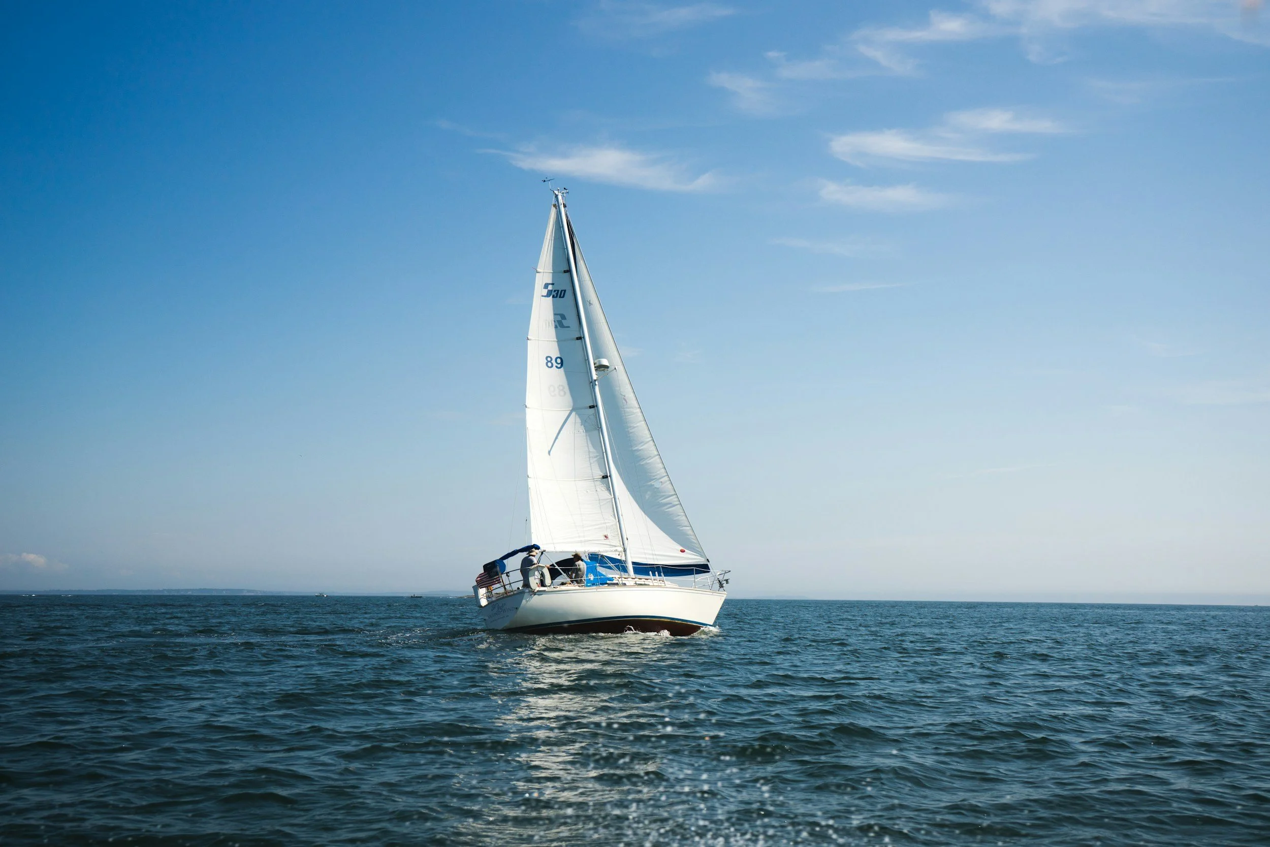 Sailboat with white sails on calm blue ocean under a clear sky.
