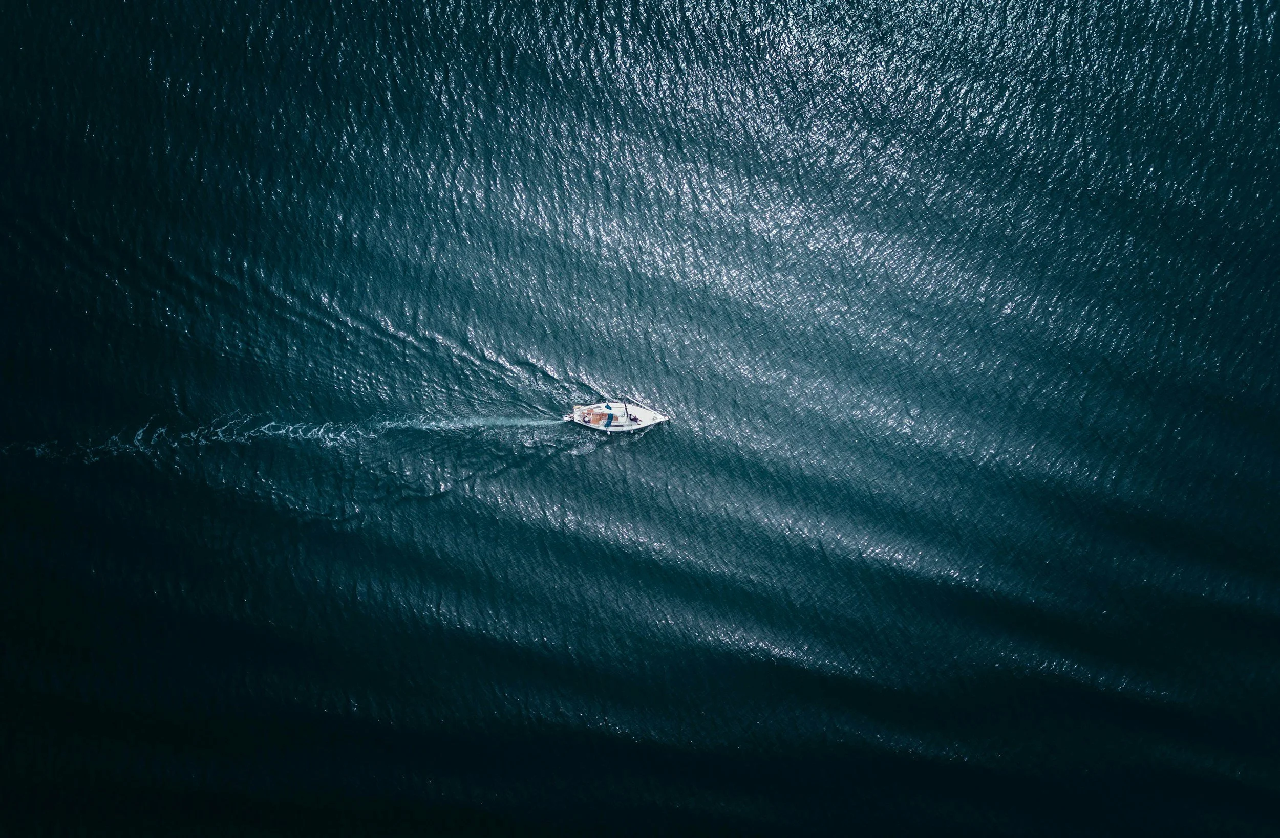 Aerial view of a boat moving through dark blue ocean water, creating white waves behind it.
