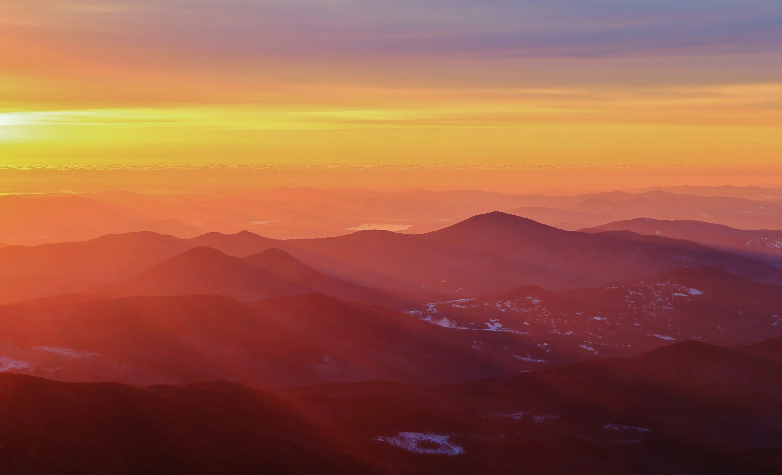 Sunset over mountain range with colorful sky and some snow patches on the mountains.