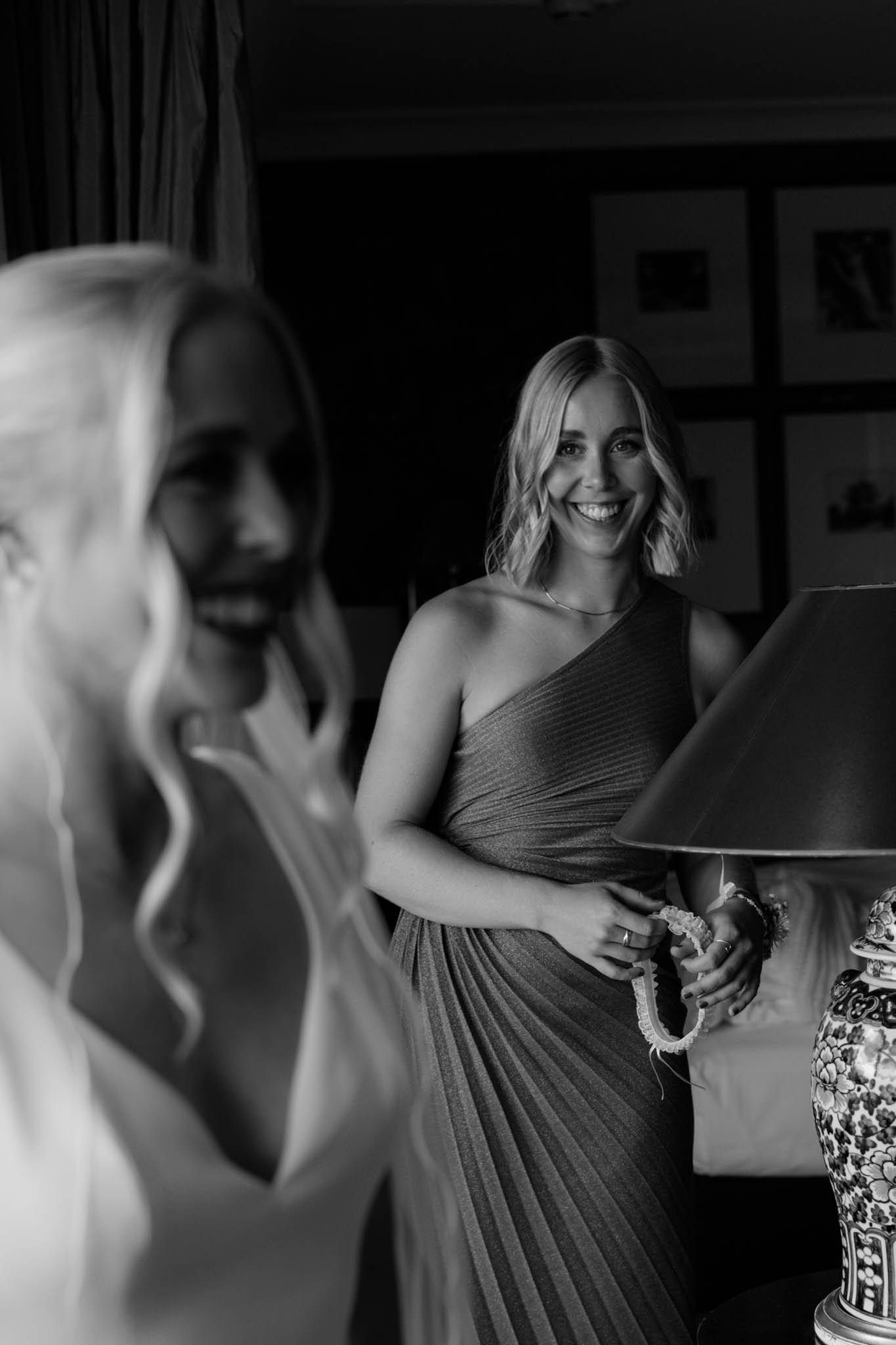 Zwei lachende Frauen in einem stilvollen Hotelzimmer im Parkhotel Bremen. Die Trauzeugin lächelt die Braut an. Man sieht die Freude in den Augen der Trauzeugin, die auch die Schwester der Braut ist.