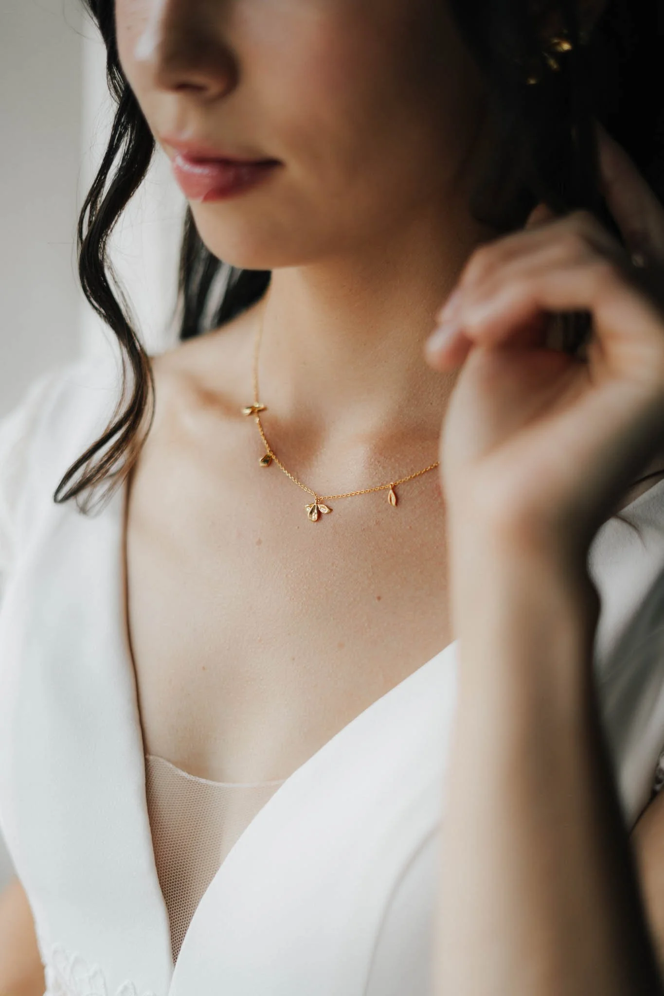 Nahaufnahme einer Frau, die eine goldene Halskette mit kleinen Anhängern trägt und sie berührt.