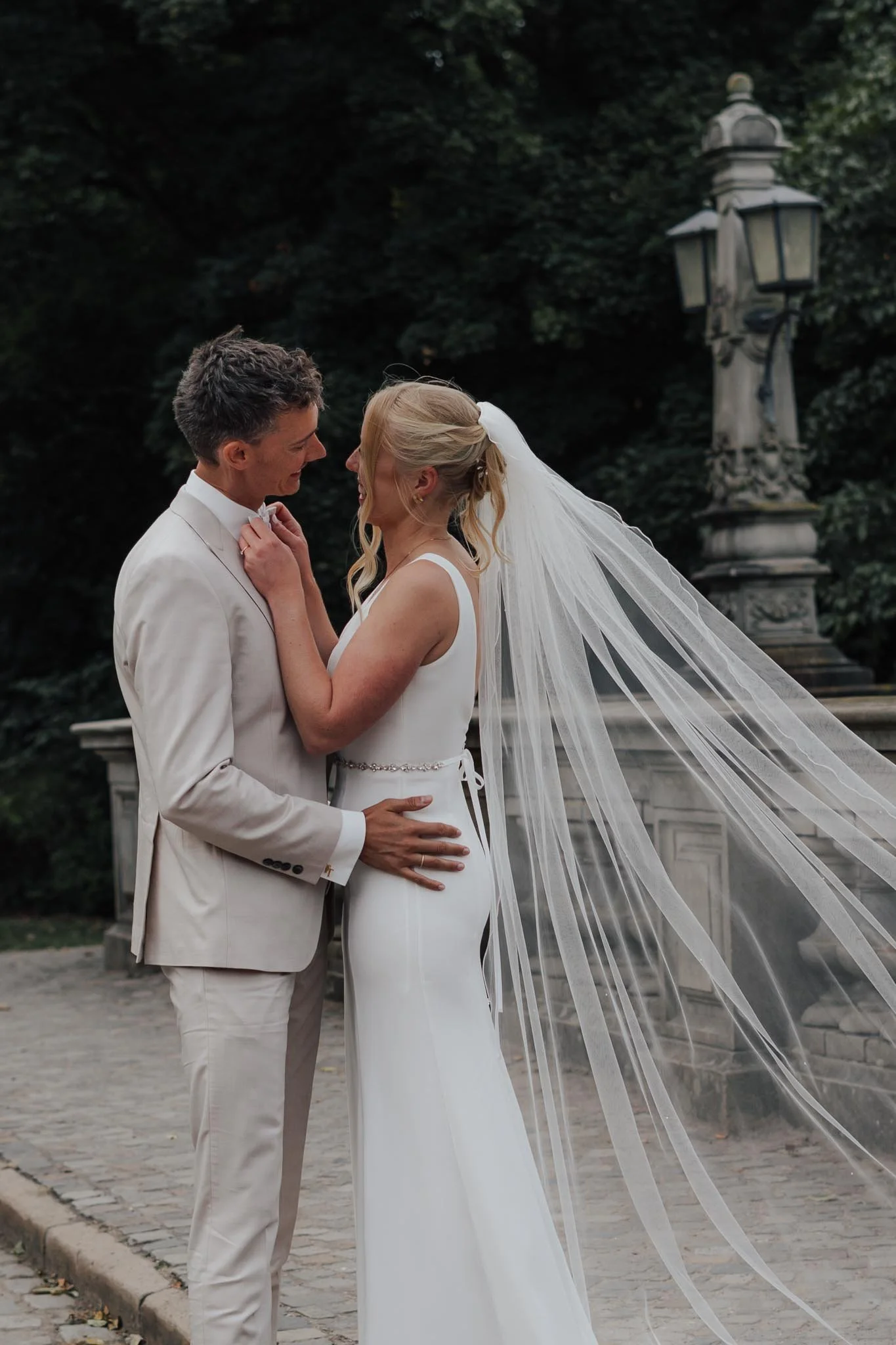 Ein küssendes Brautpaar, das beim Paarshooting im Bürgerpark in Bremen gegenüber steht. Die Braut trägt einen weißen Schleier, der im Wind weht. Die Szene zeigt die Liebe zwischen ihnen.