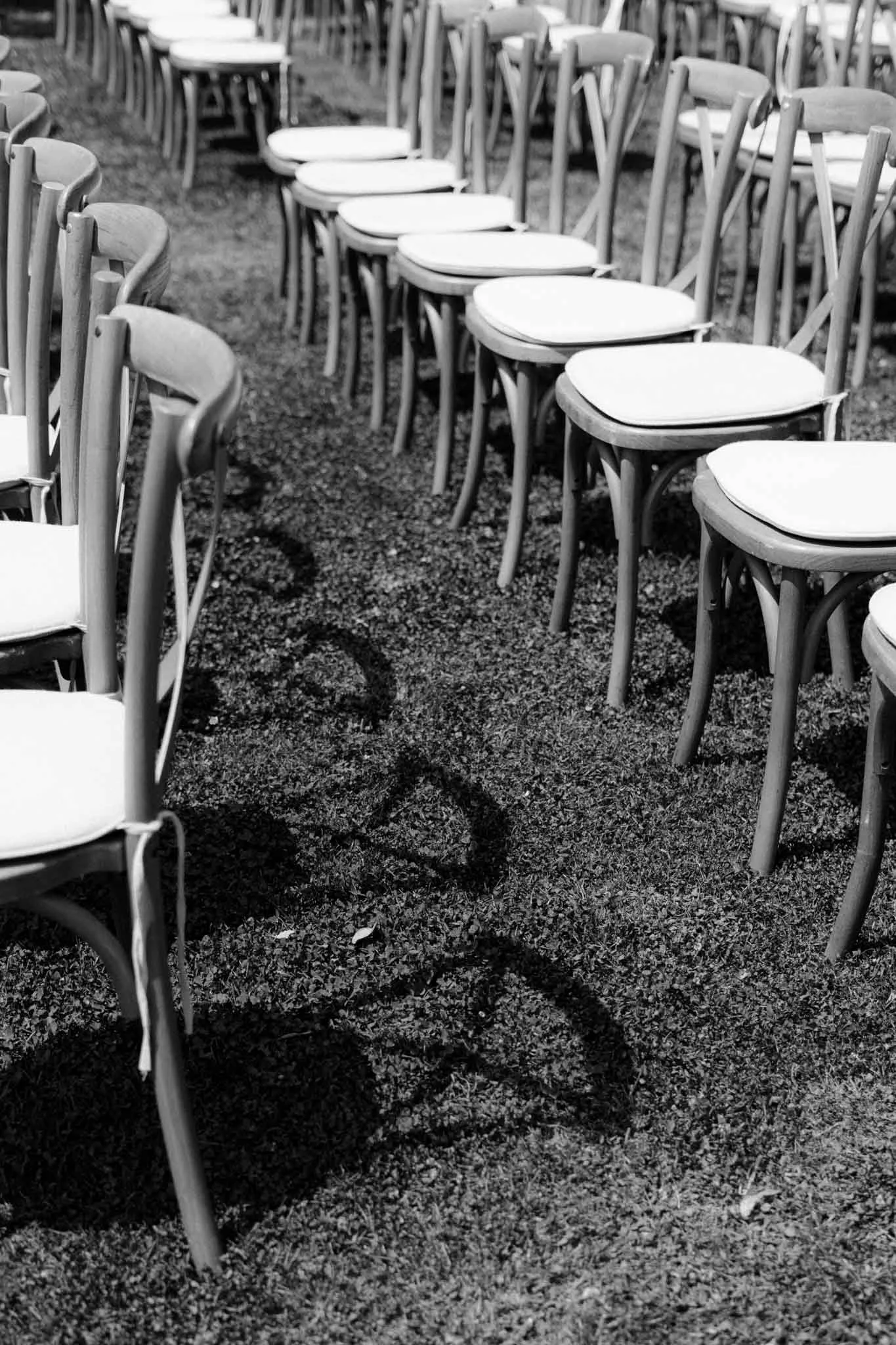 Mehrere leere Stühle in kunstvoller Reihen auf einem Boden, schwarz-weiße Aufnahme.