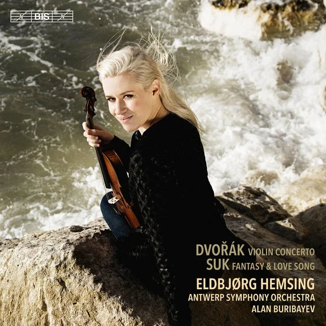 A woman with platinum blonde hair sitting on rocks by water, holding a violin, looking at the camera, promotional text for a classical music concert.