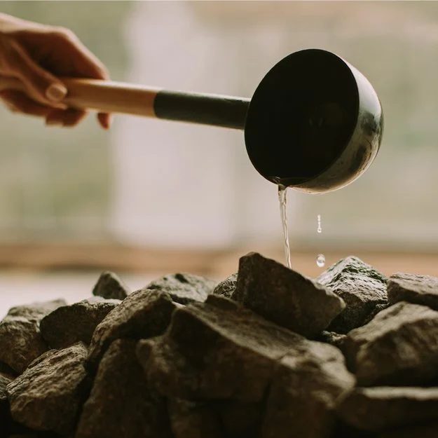 Une main tenant une louche en métal au-dessus d'une pile de pierres, avec de l'eau qui s'écoule de la louche.
