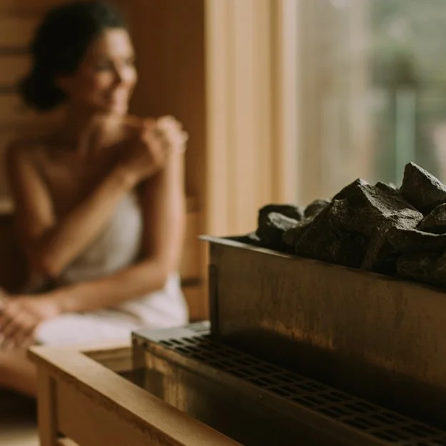 Une femme souriante assise près d'une cabine de sauna ou de cheminée avec des pierres