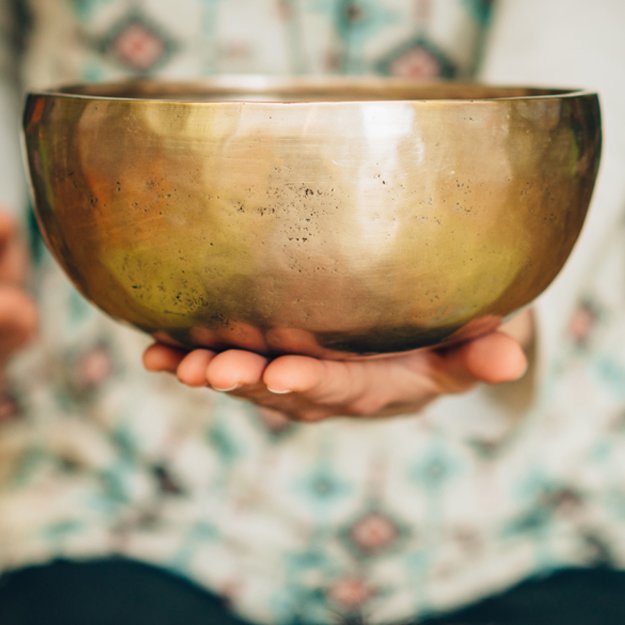 Une personne tient une grande coupe en métal doré, le fond est flou et montre une personne en chemise à motifs floraux.