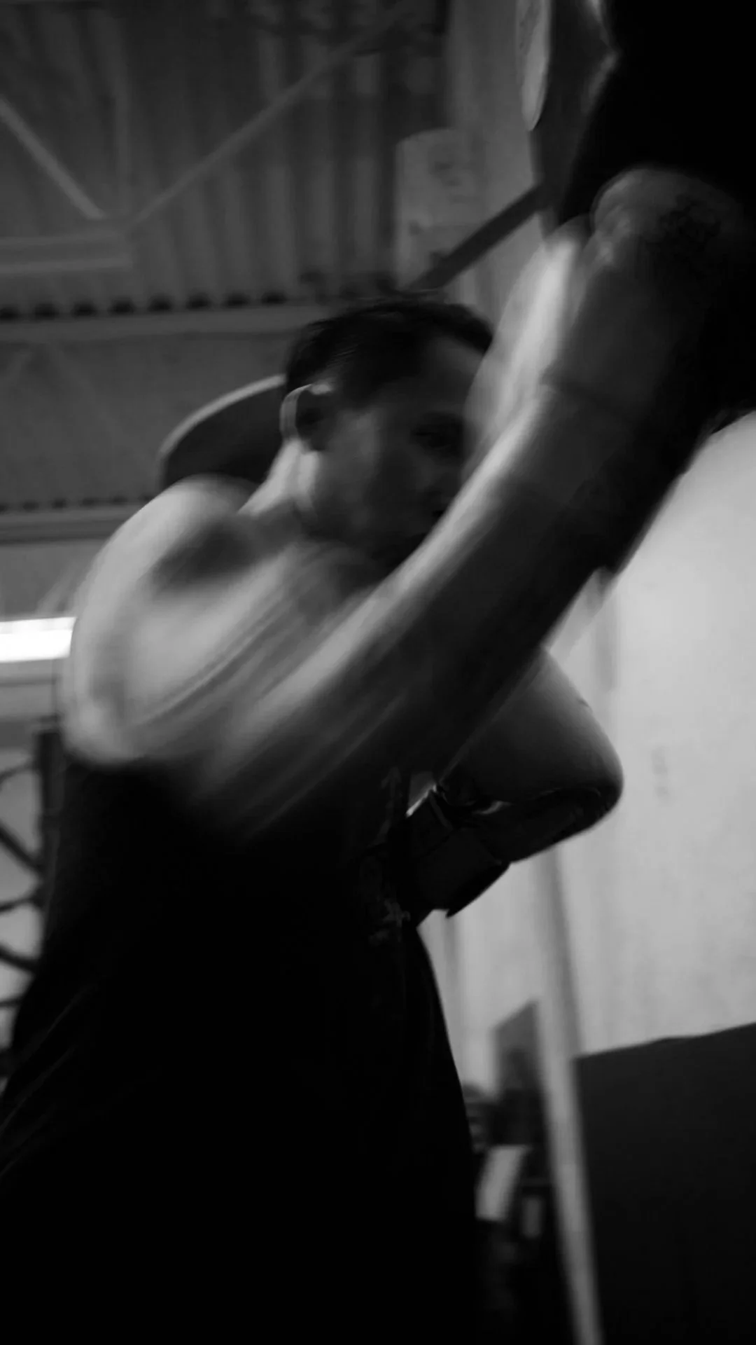 A person lifting a dumbbell in a gym, captured in black and white.