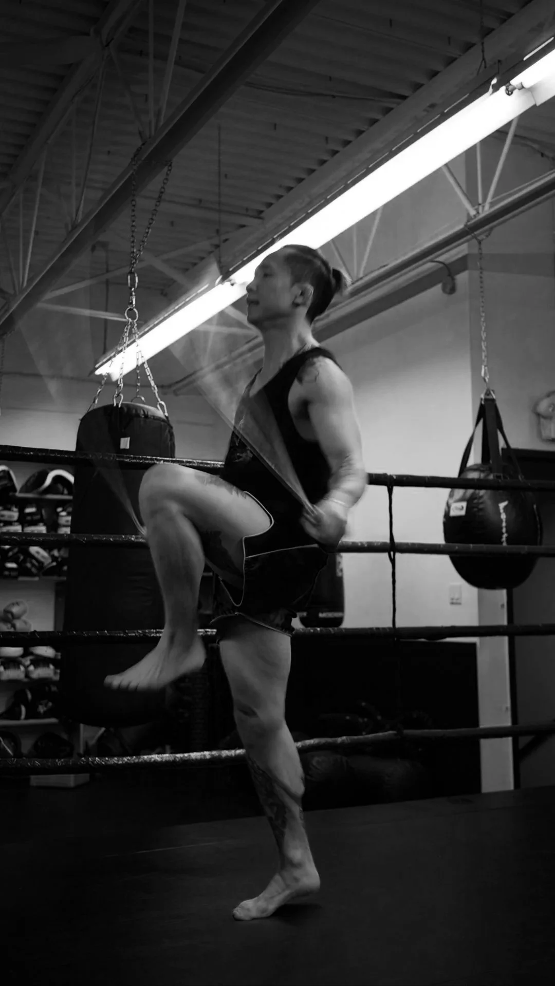 A woman training in a boxing gym, kicking a punching bag while playing a guitar.