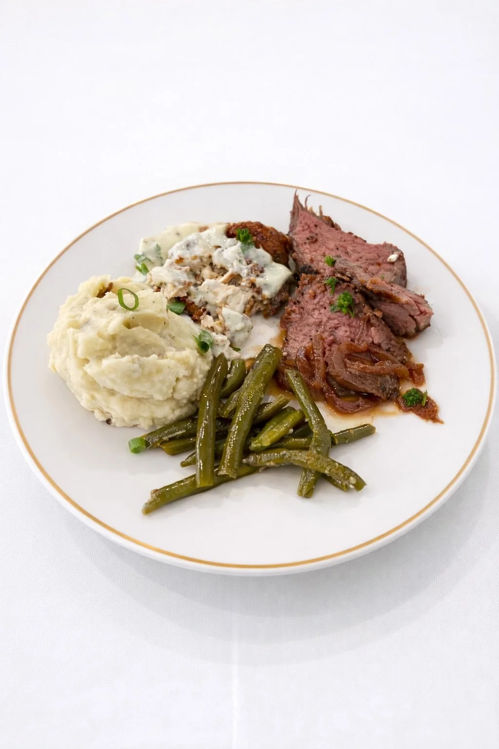Plate of food with mashed potatoes, green beans, roast beef with gravy, and a meat dish topped with white sauce and herbs.