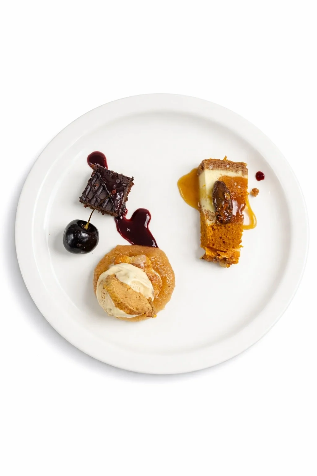 Plate with three assorted desserts: a chocolate brownie with red sauce, a cherry, a scoop of vanilla ice cream with a cookie, and a layered pastry with caramel and cream, garnished with fruit sauces.