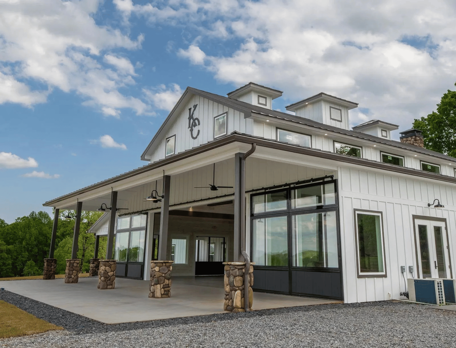 White modern barn-style building with stone pillars, large windows, and a covered porch, under a partly cloudy sky.