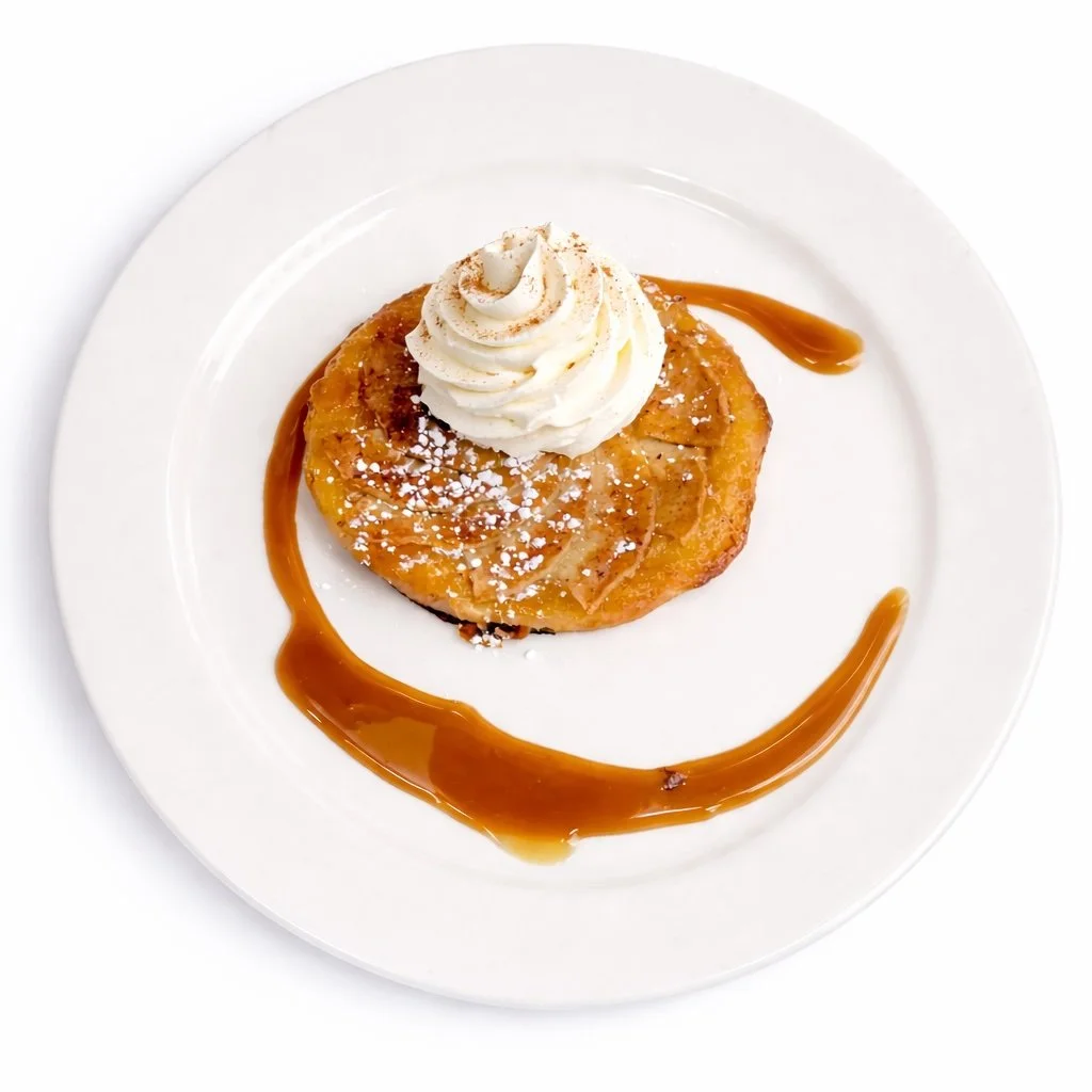 Dessert plate with caramelized apple tart, whipped cream topping, caramel sauce drizzle, and powdered sugar