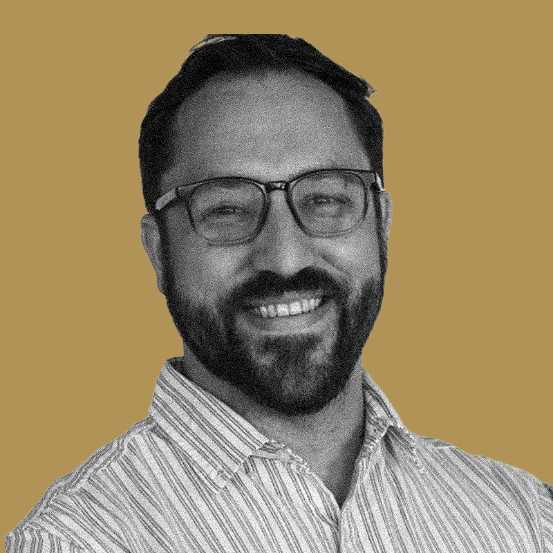 Portrait of a smiling man with glasses and a beard wearing a striped shirt, set against a plain background.