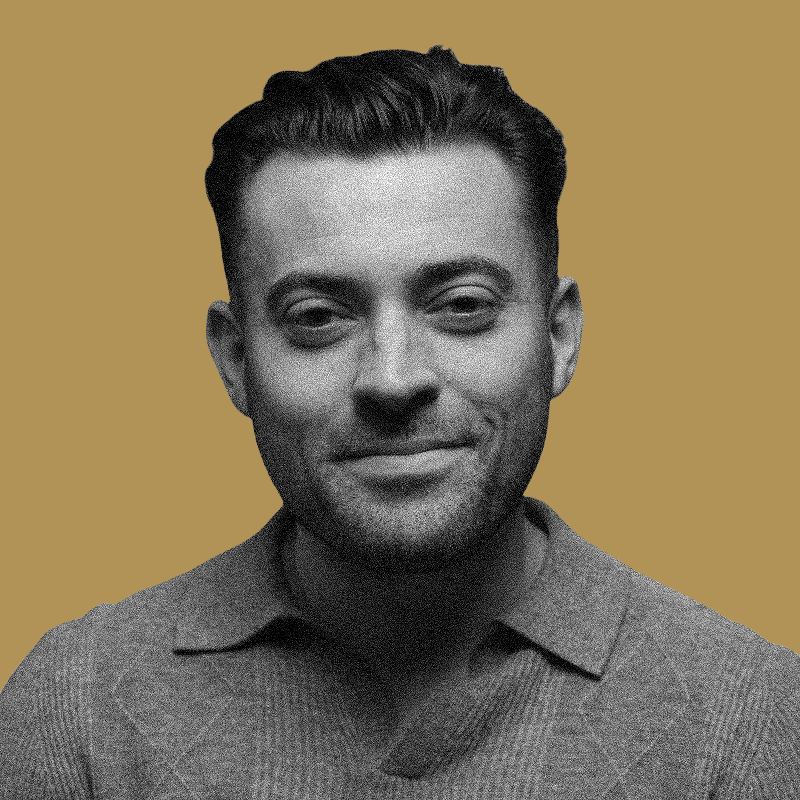 Black and white portrait of a man smiling, wearing a collared shirt, with a plain light brown background.