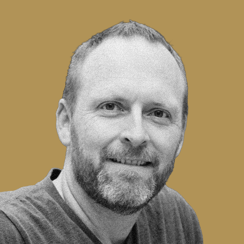Black and white portrait of a smiling man with short hair and beard, wearing a casual shirt, against a plain background.
