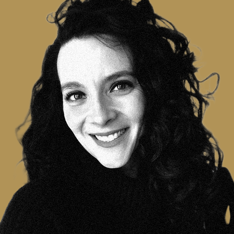 A woman with long curly black hair smiling at the camera against a plain beige background.