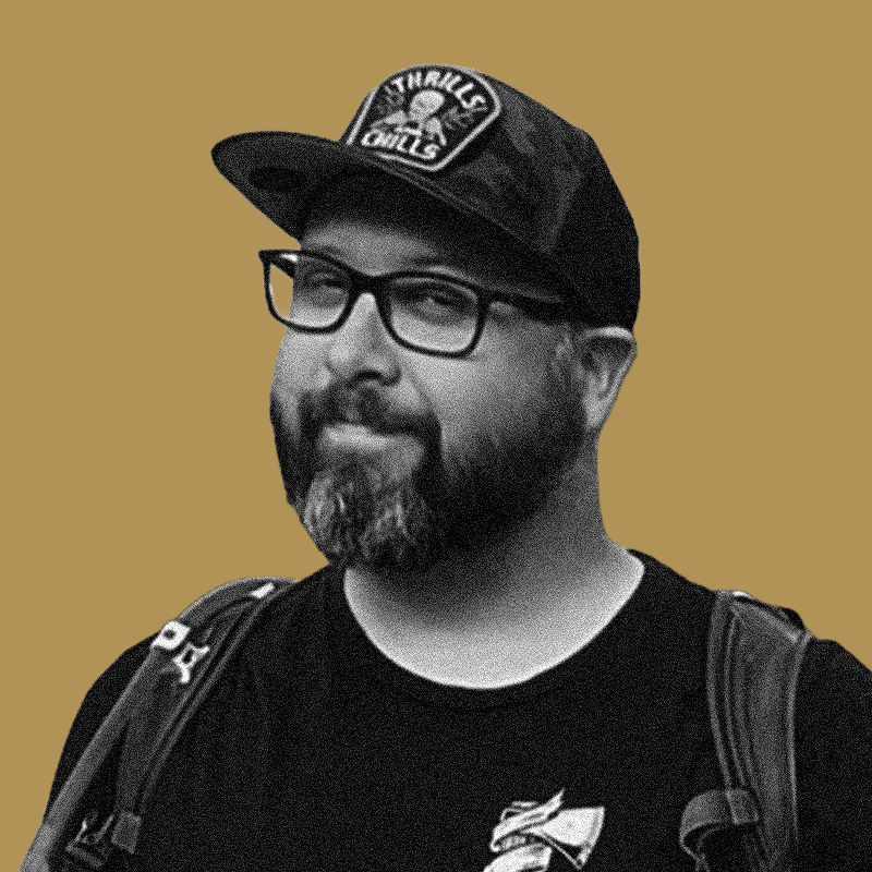 A man with glasses, a beard, and a cap that says 'Steel Tactics'.