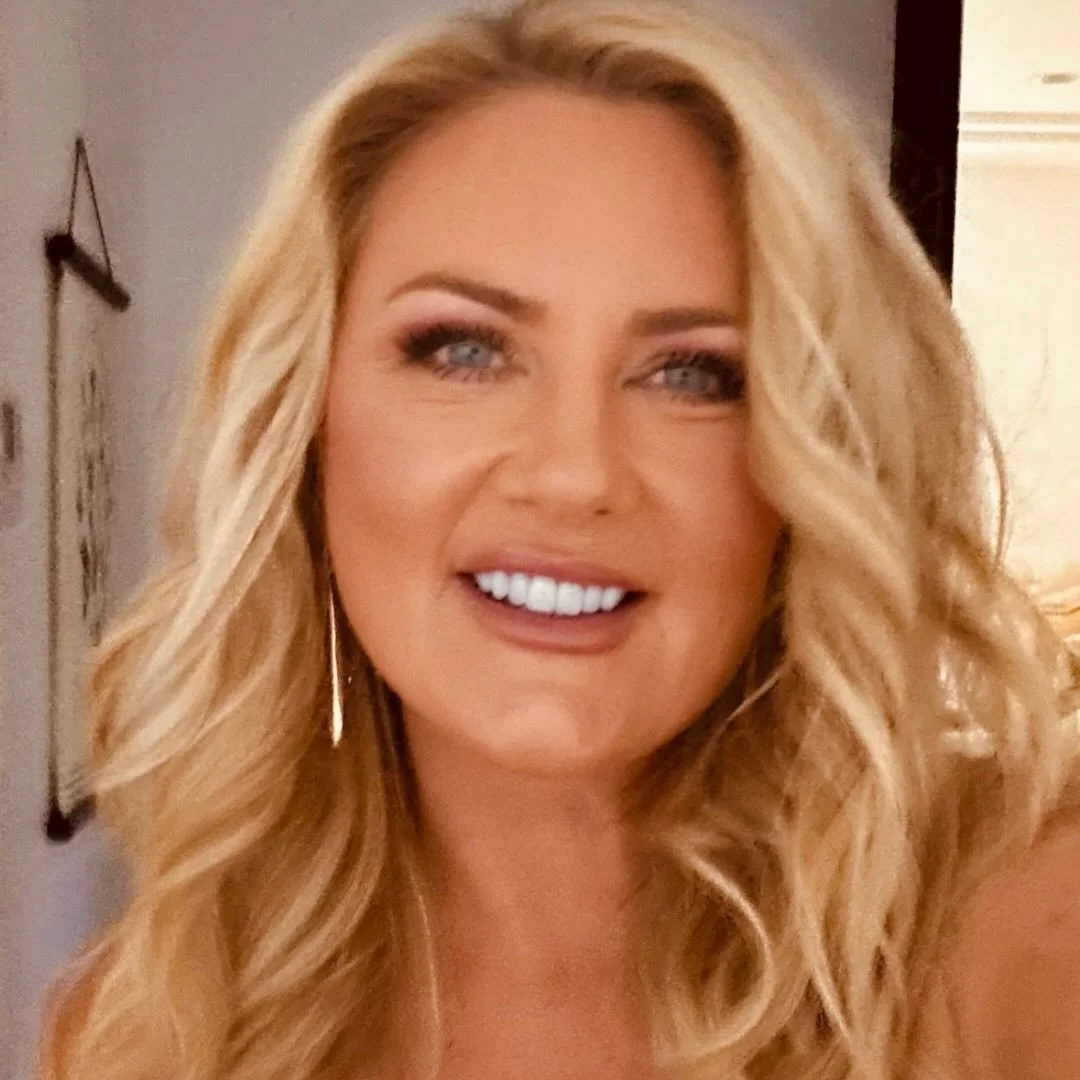 A smiling woman with long, wavy blonde hair and blue eyes.