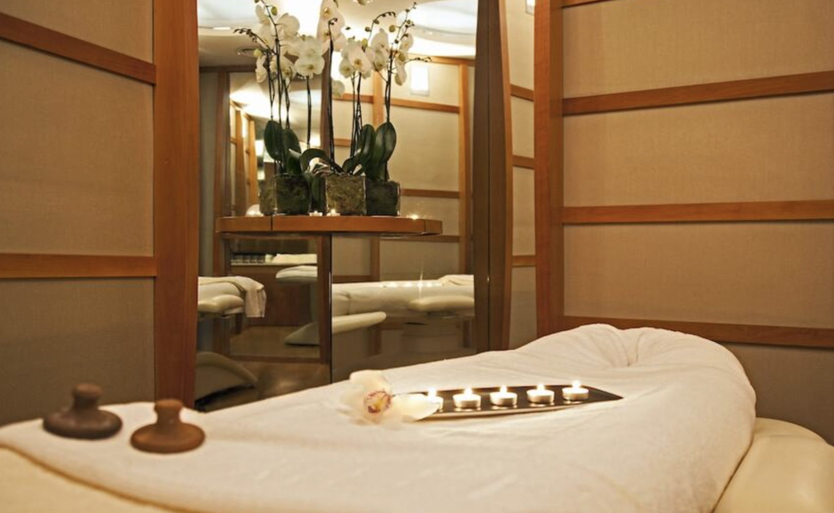 Spa room with a massage bed, candles, and orchids.