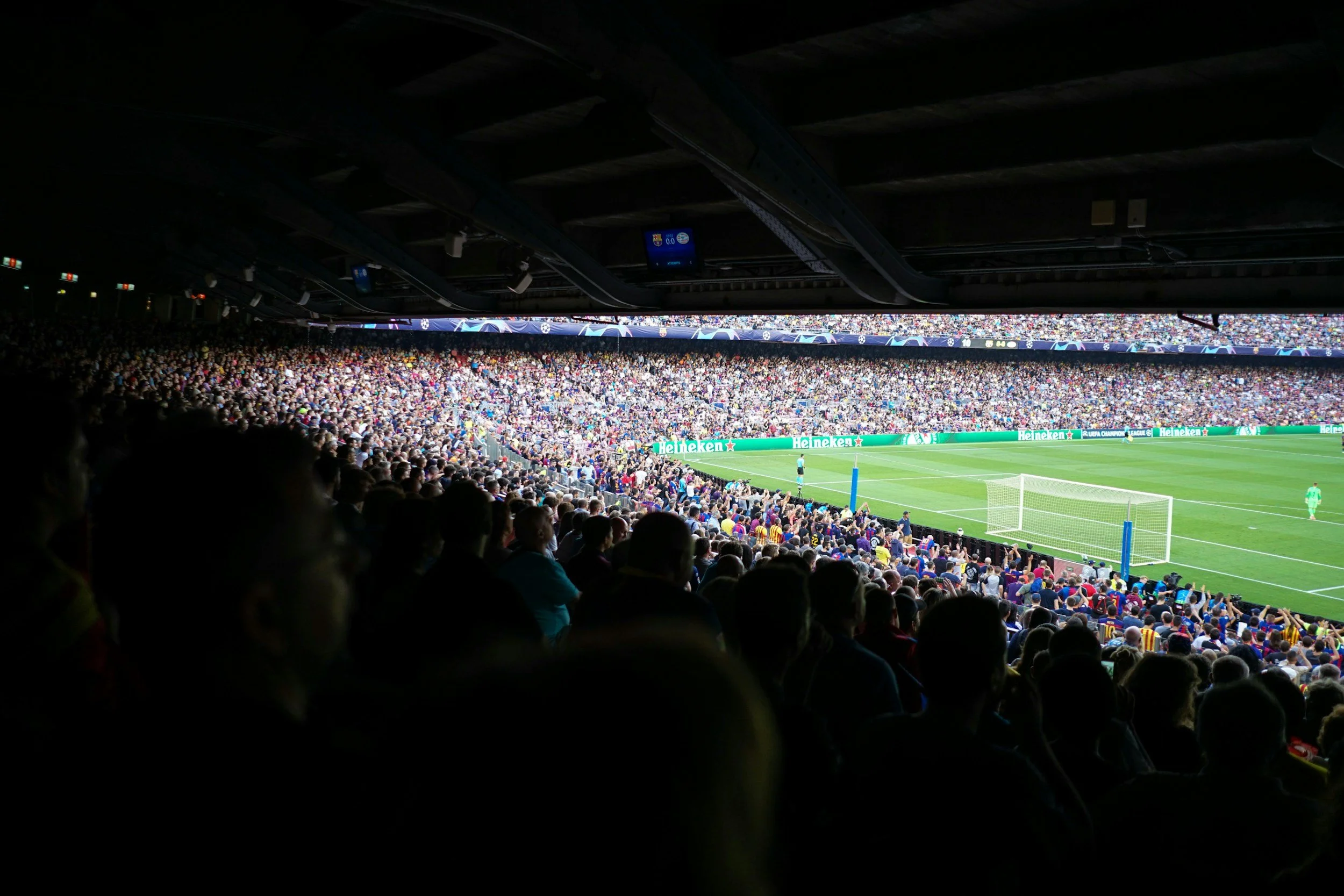 View of a crowded soccer stadium from the perspective of a spectator in the stands, showing players on the field and spectators in the background.