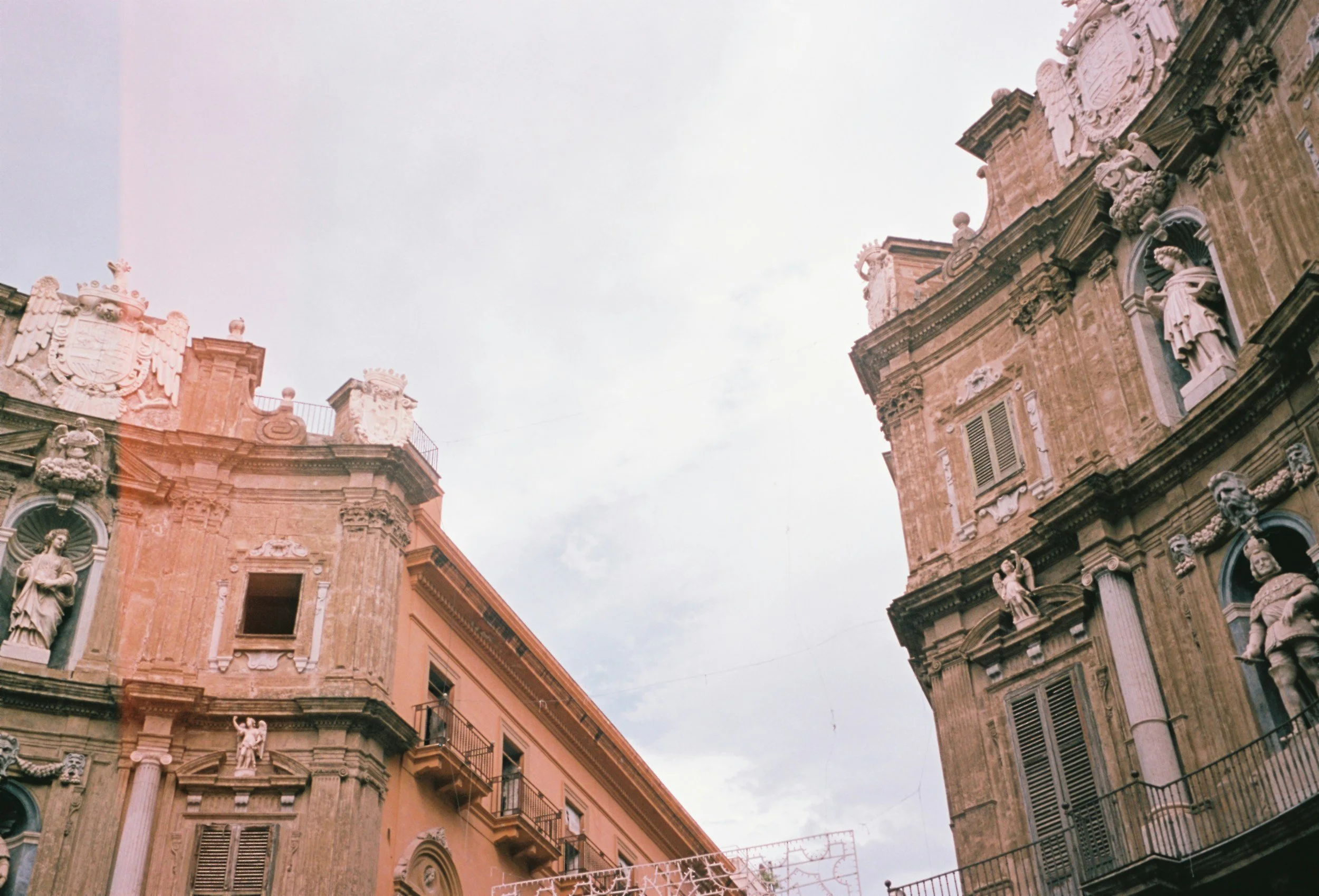 Historical European-style buildings with intricate sculptures and statues on facades, set against a cloudy sky.