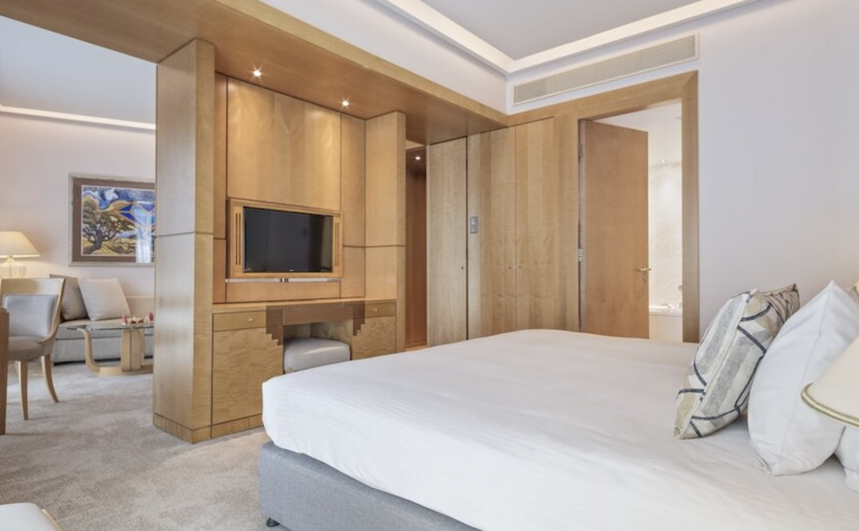 Luxury hotel room with a bed, a wooden partition with a TV, and a sitting area with a painting on the wall.