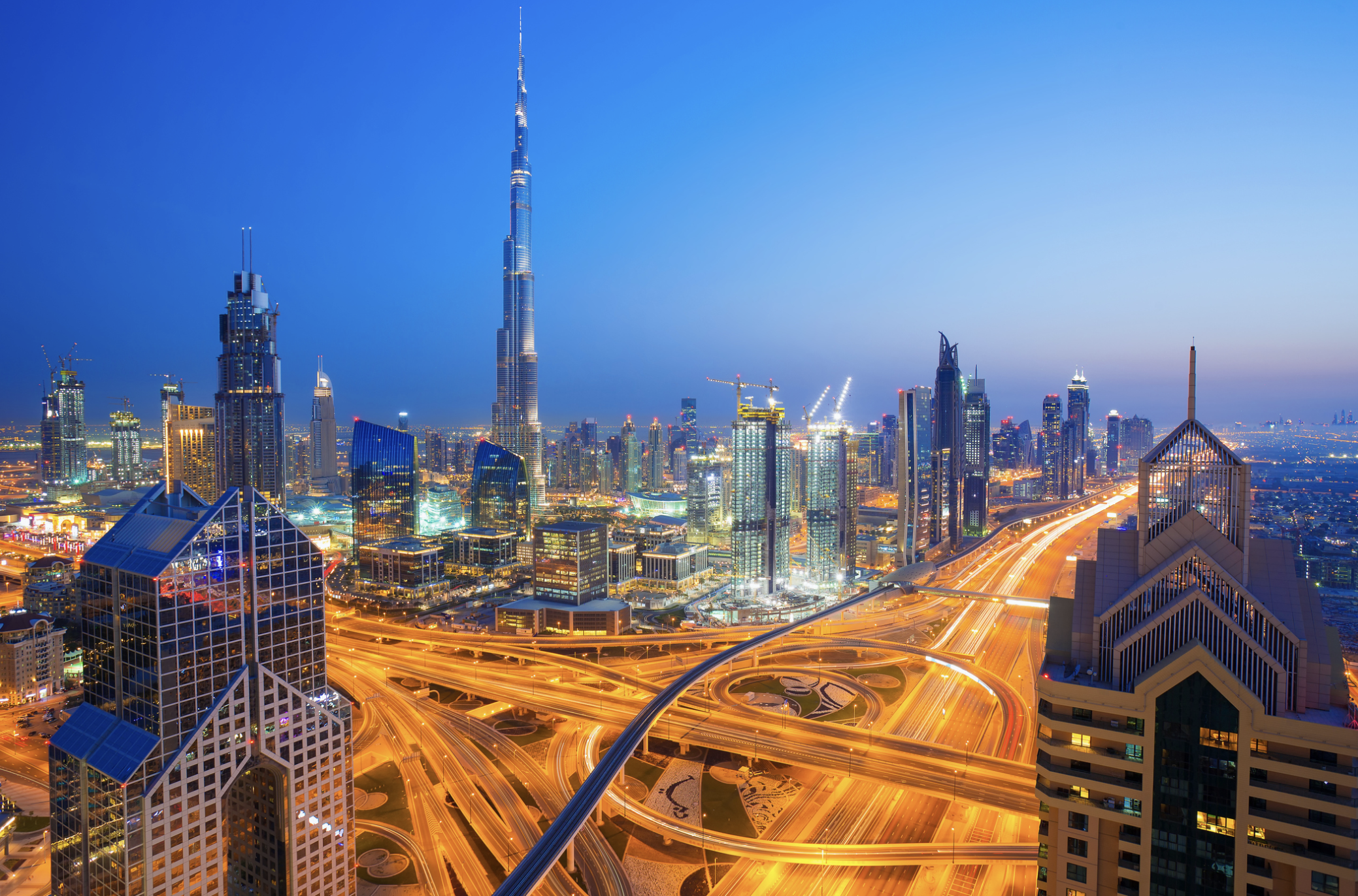 Night view of Dubai skyline featuring the Burj Khalifa with highways illuminated and surrounding skyscrapers.