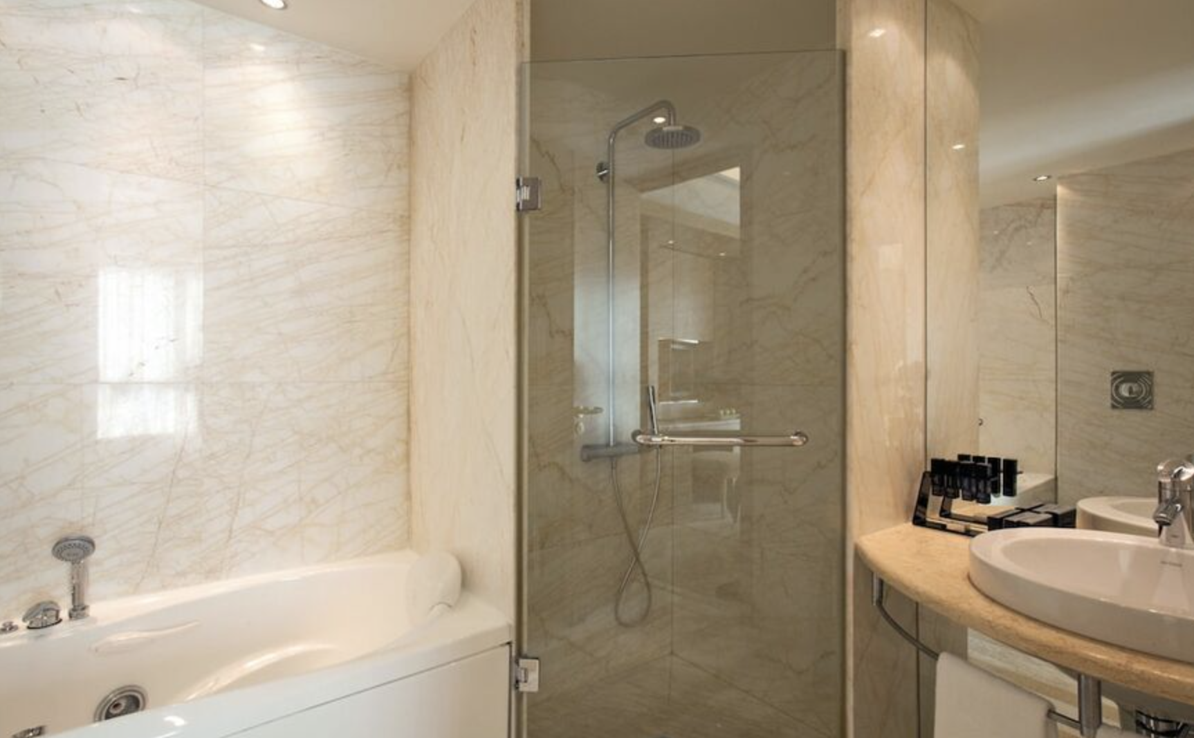 Bathroom with a whirlpool bathtub, a glass-enclosed shower with a handheld showerhead, and a sink with toiletries on the countertop.