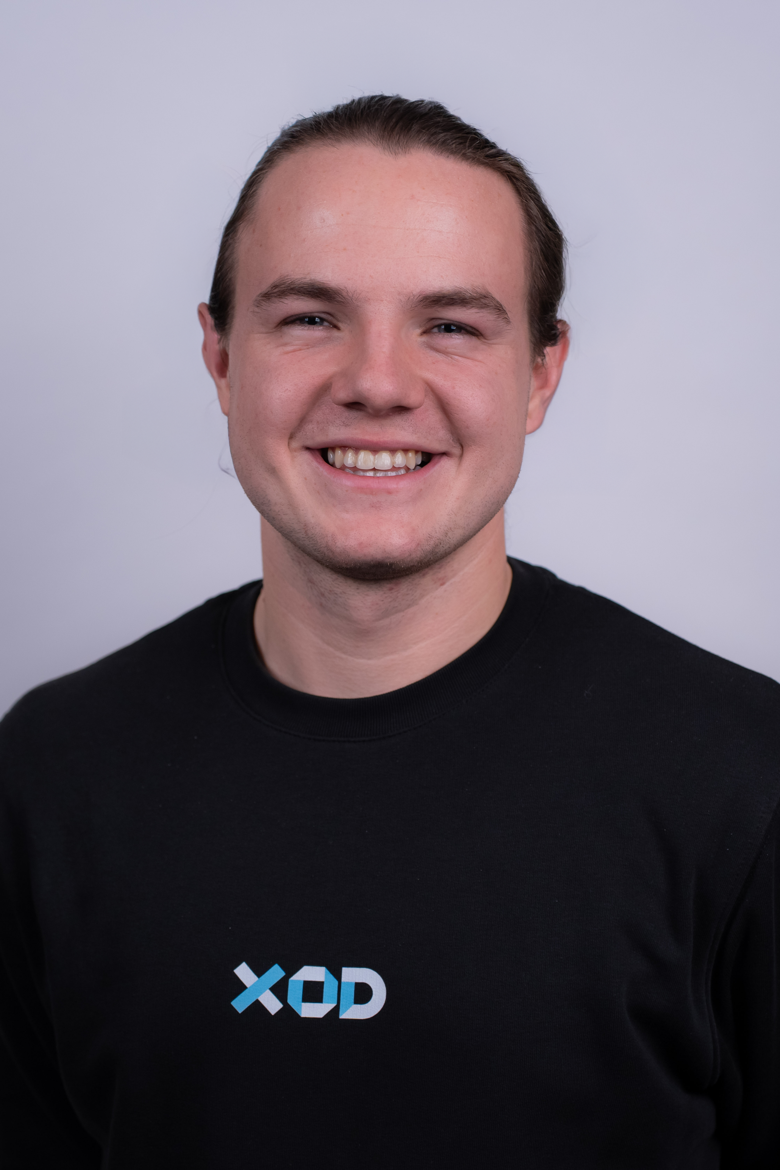 A smiling woman with glasses, hoop earrings, layered necklaces, and curly hair.
