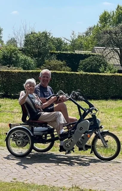 An elderly man and woman riding a motorized tricycle outdoors on a sunny day, smiling and enjoying the moment.