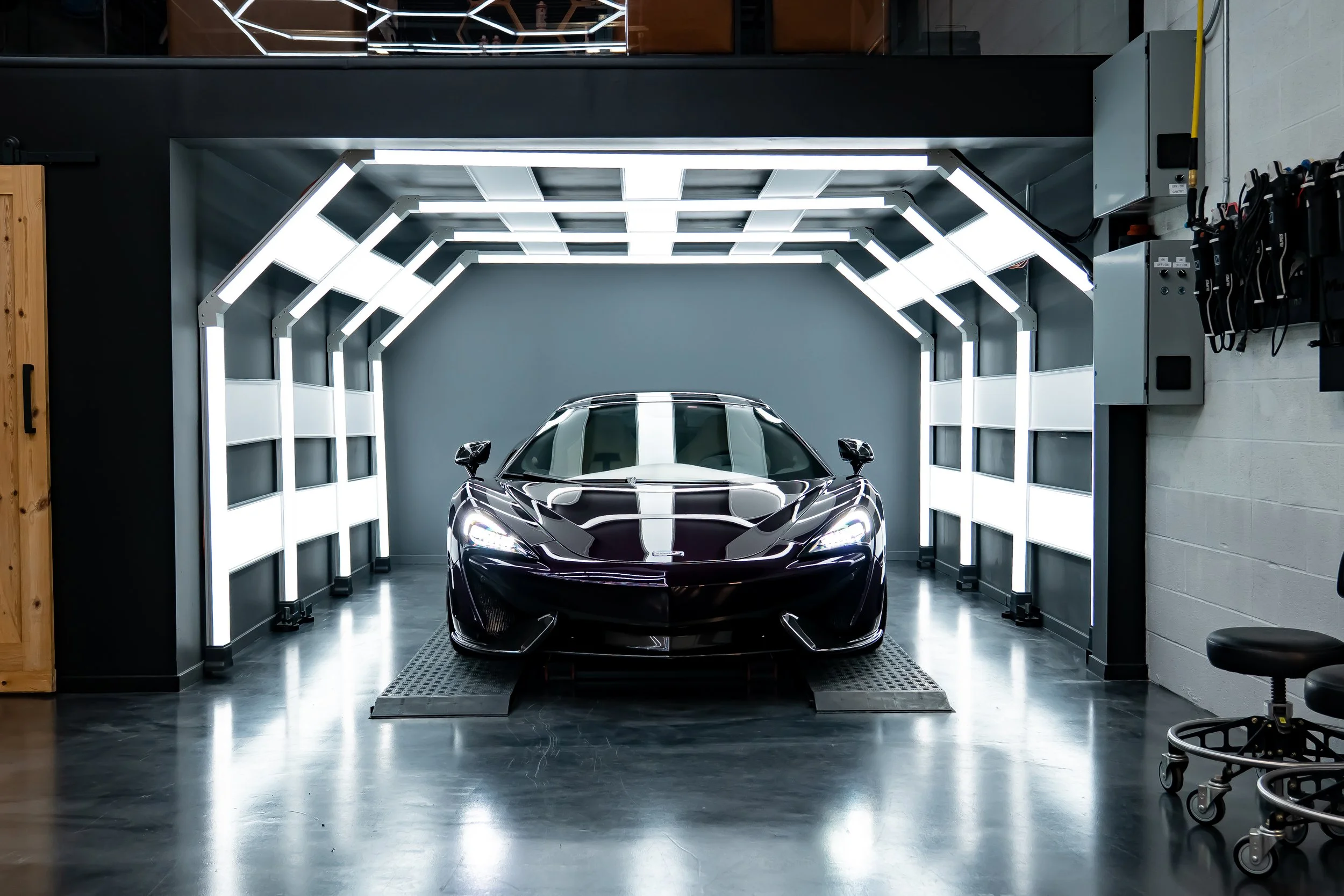 A sleek purple Mclaren 570S on a hydraulic car lift inside ZAutoCare's purpose built, 360 degree ceramic coating light tunnel in Waterloo, ON.