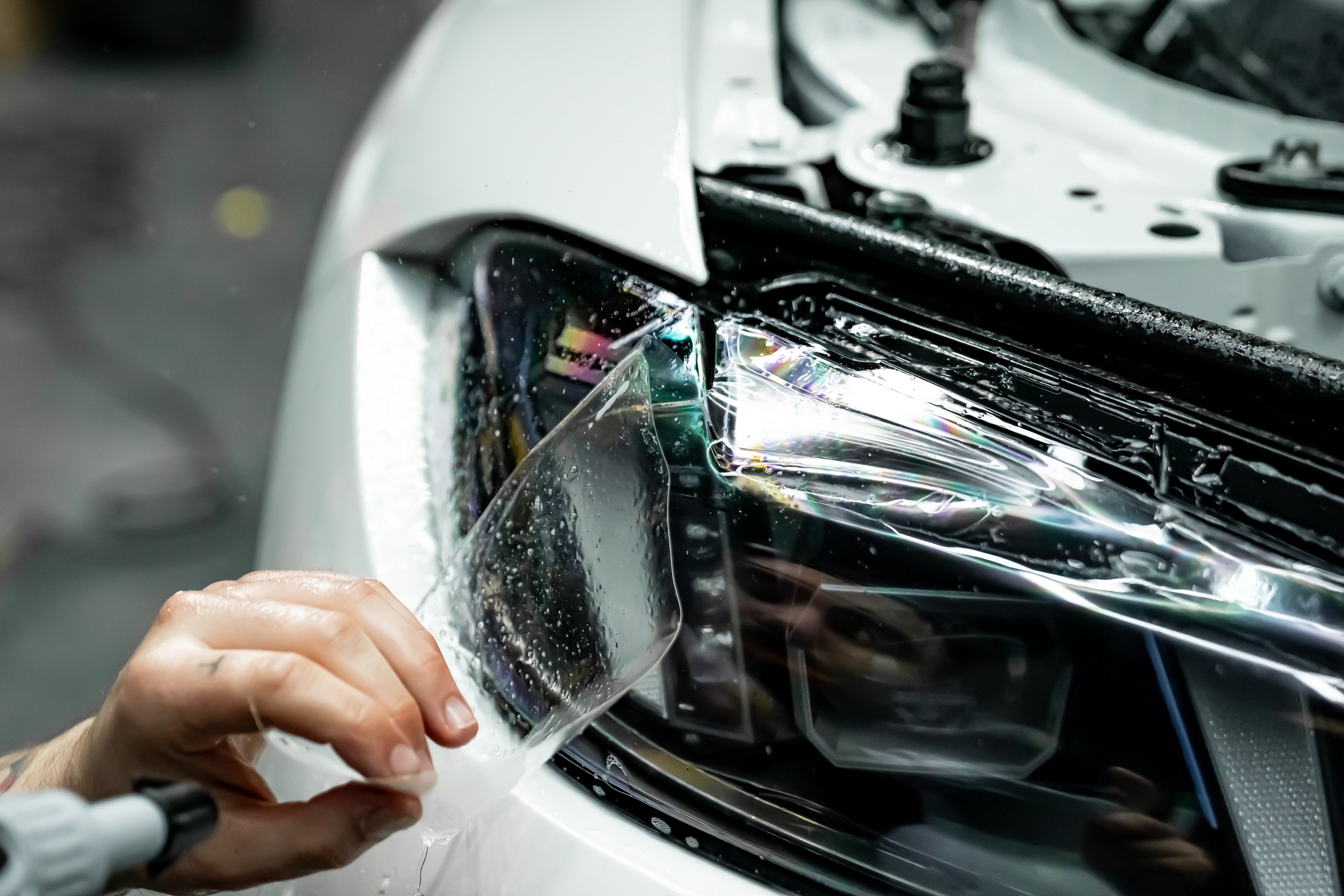 Technician installing premium paint protection film on a vehicle headlight as part of a professional PPF application.