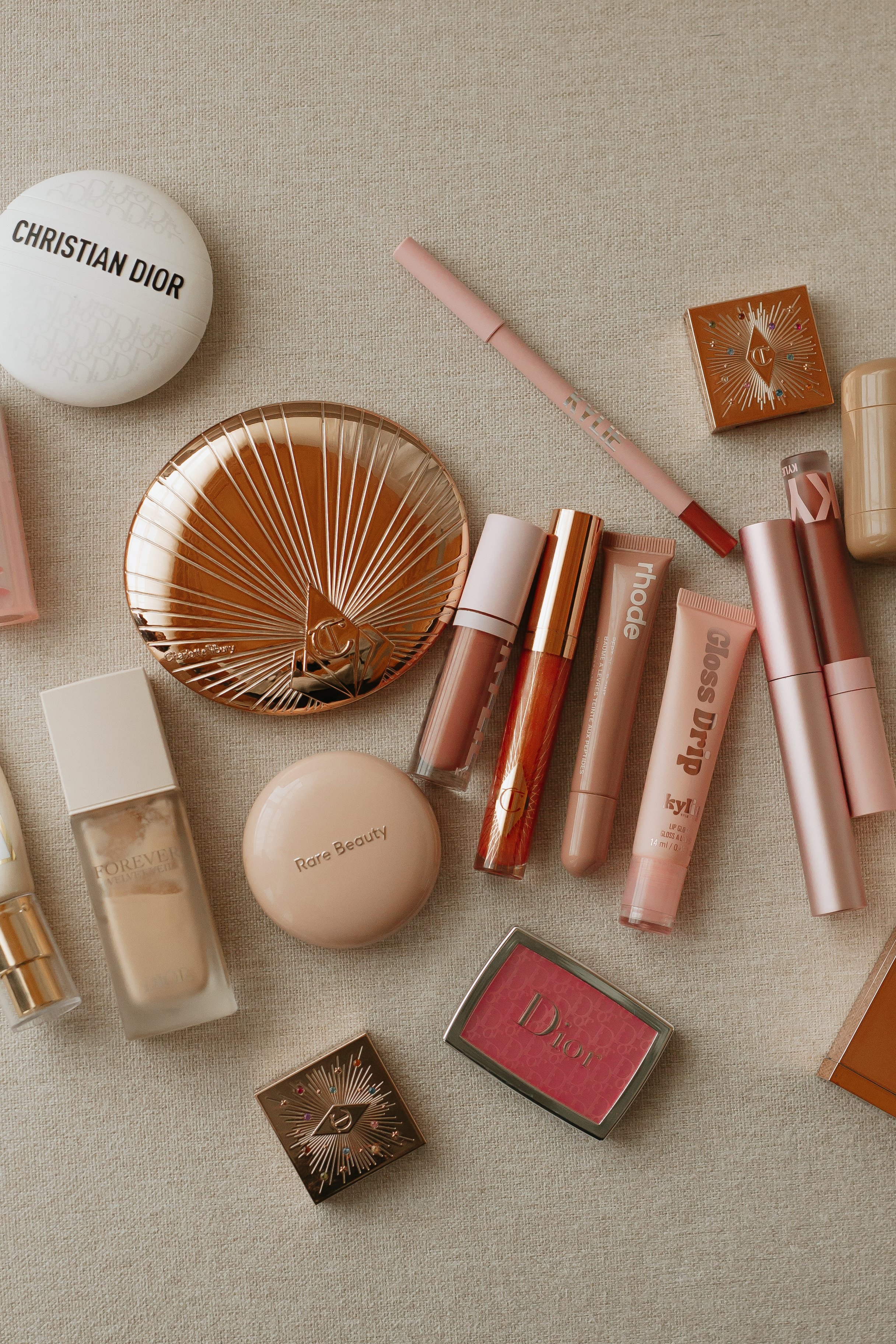 A collection of makeup and skincare products, including lipstick, blush, perfume, and decorative containers, arranged on a light-colored surface.
