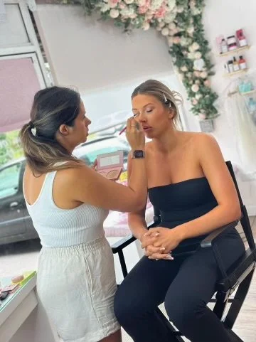 Makeup artist applying makeup to a woman sitting in a makeup chair in a beauty salon with floral decor