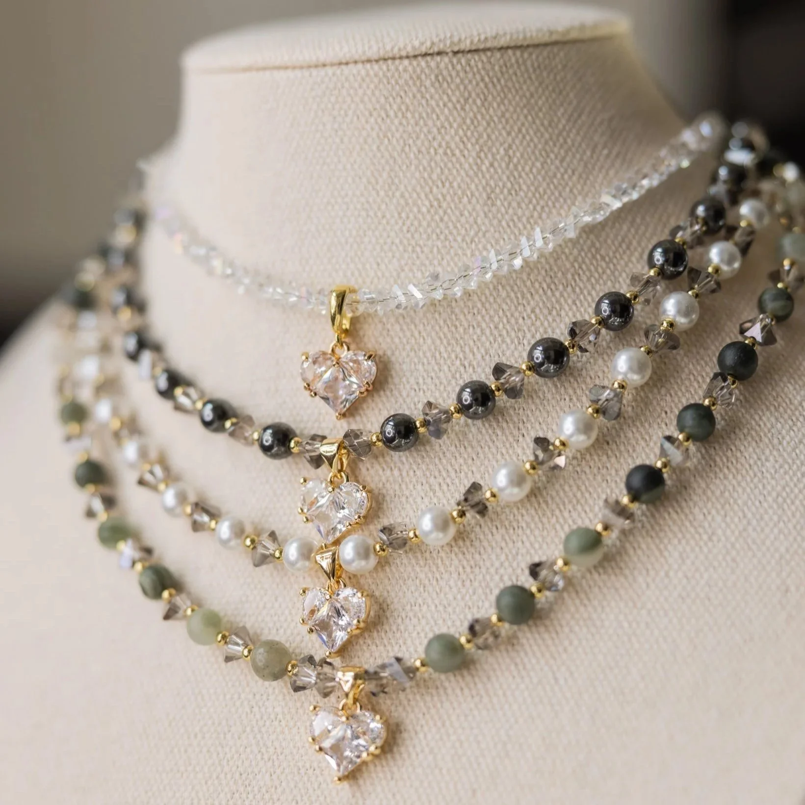 Collection of layered necklaces with black, white, and gray beads and gold accents, displayed on a beige jewelry stand.