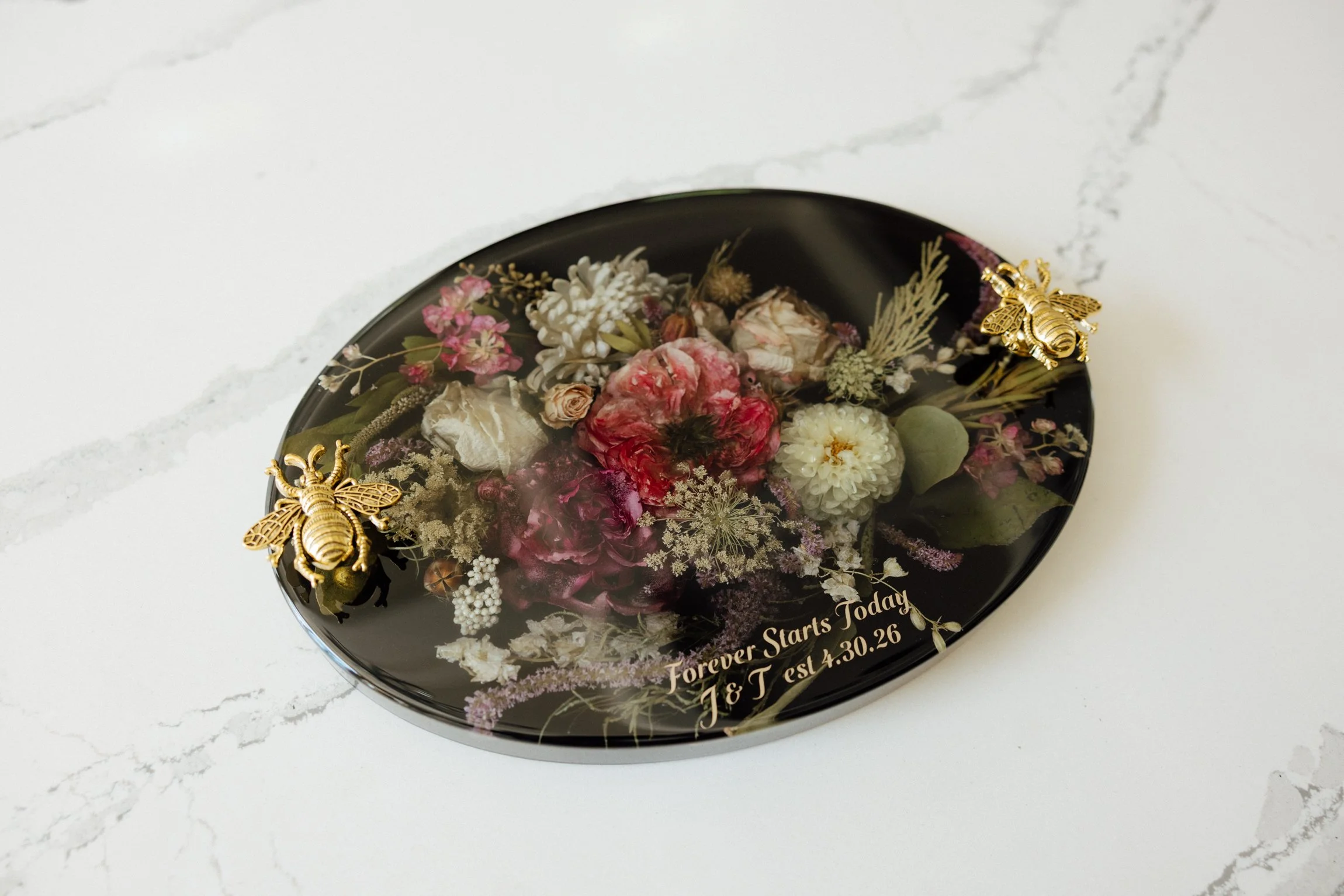 Decorative black oval tray with dried flowers and gold bee ornaments, inscription reads "Forever Starts Today J & T est 4.30.26".